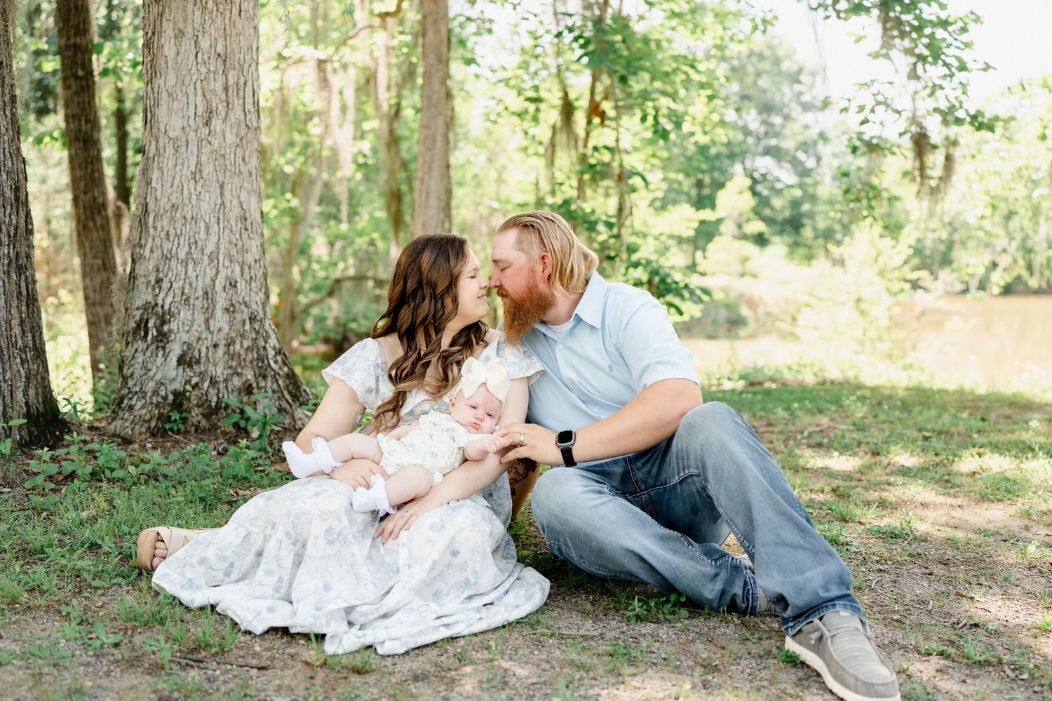 Natural light filters through trees as family sits together for outdoor portraits.