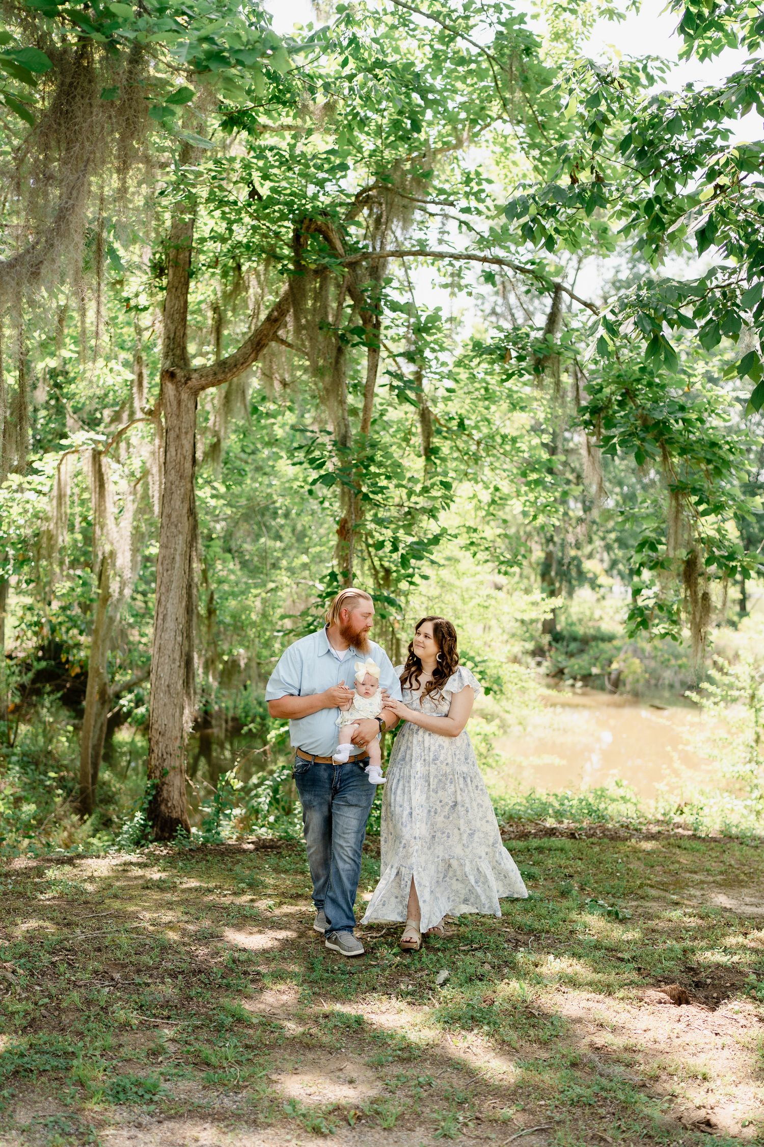 Family of three walks and poses together in scenic wooded area with dappled sunlight.