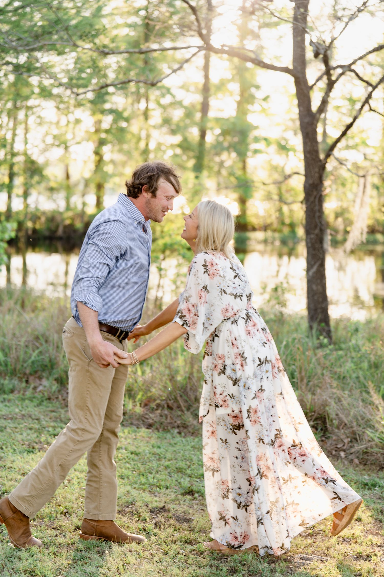 Playful couple dancing in nature wearing a floral maxi dress and blue button-down shirt.