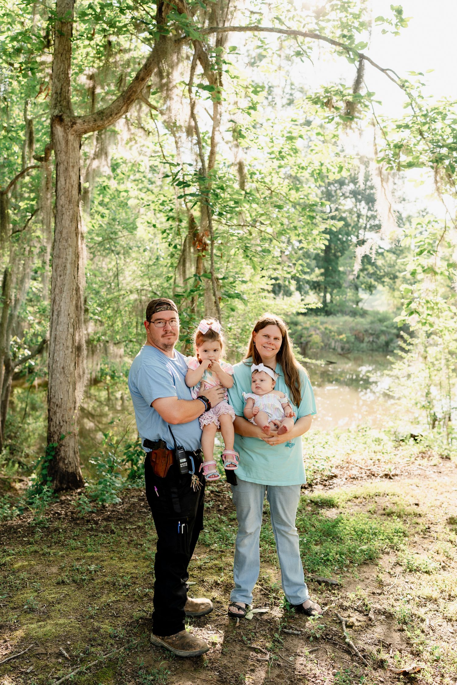 Young family with small children posing together in a sunlit forest clearing.
