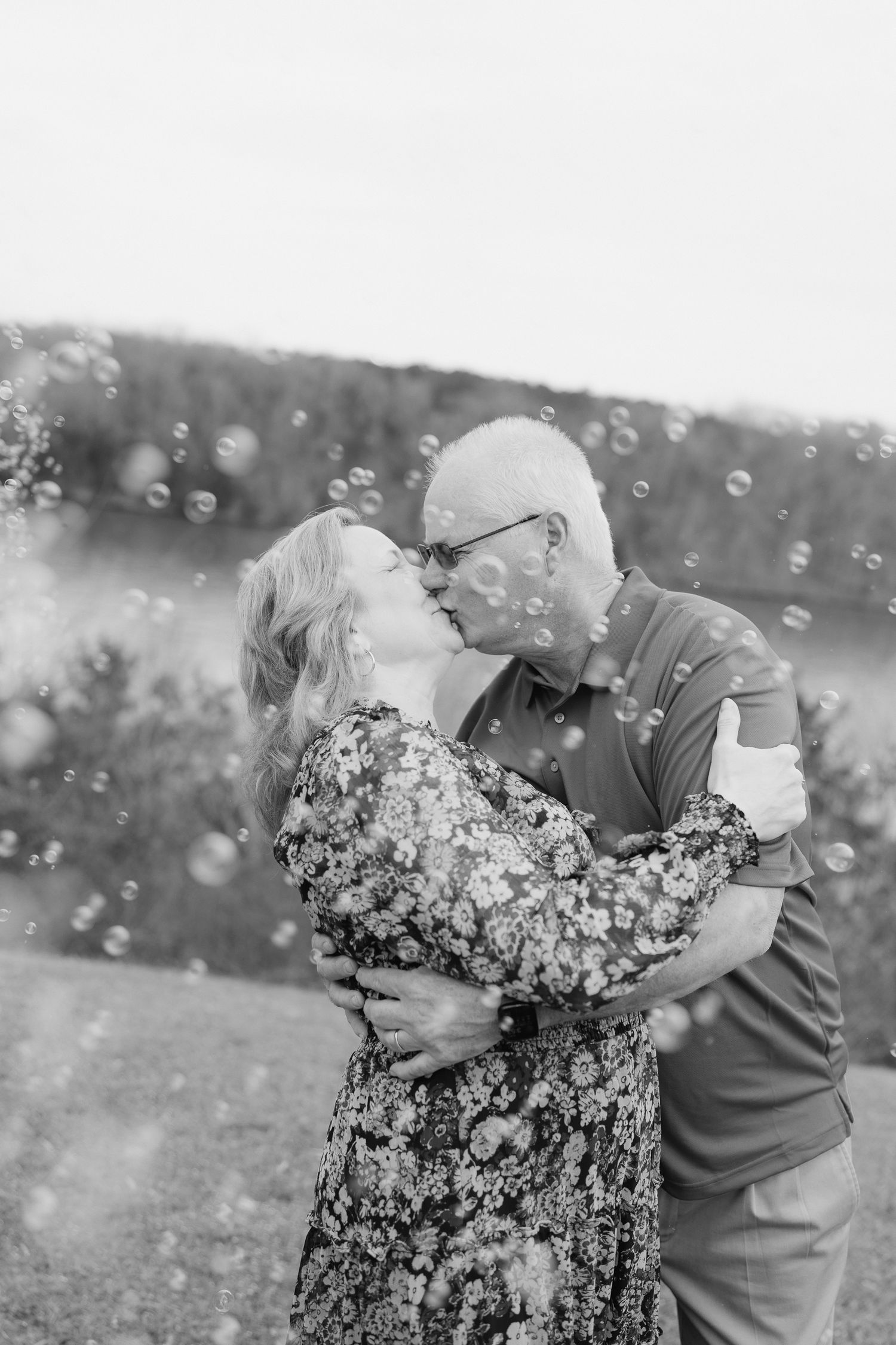 Romantic black and white photo of an older couple kissing surrounded by floating bubbles outdoors.