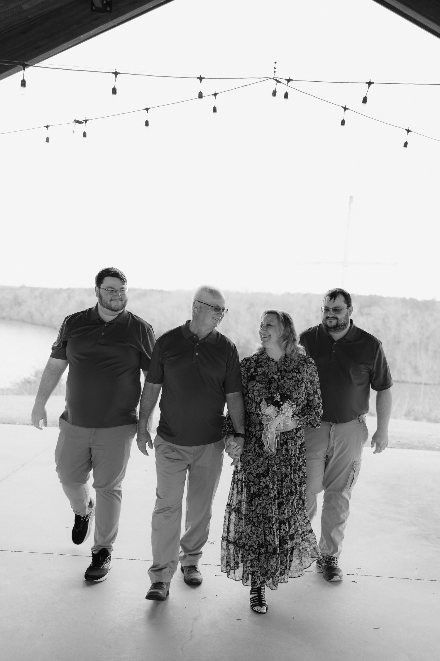 Family of four walks together laughing under string lights in an open-air venue.