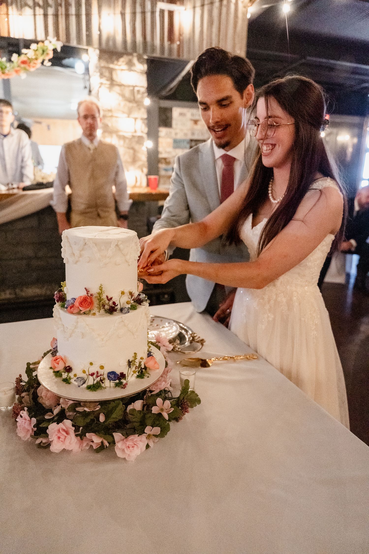 A series of photos showing a wedding couple cutting their elegant white tiered cake decorated with pink roses.