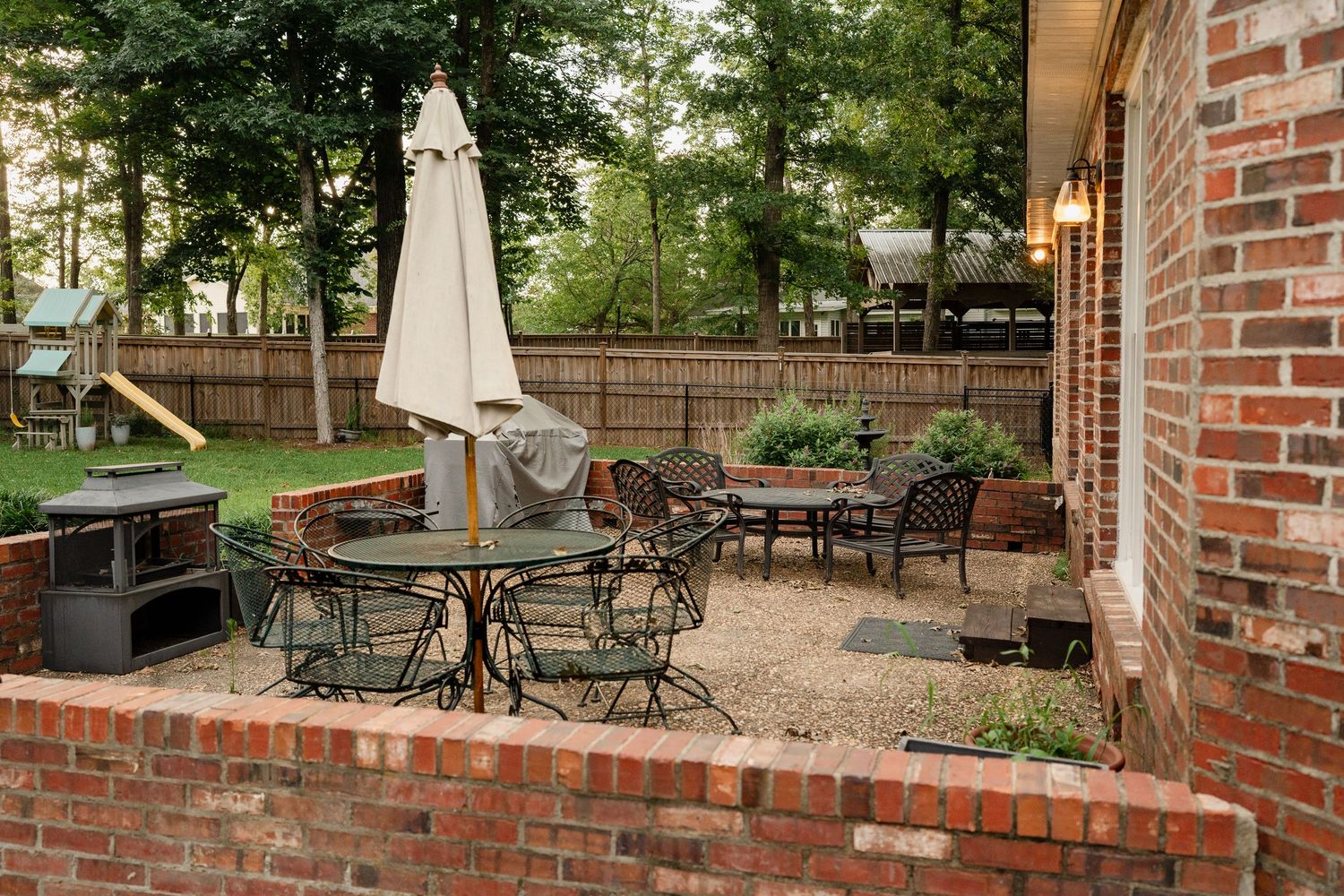 Brick patio area with outdoor dining furniture and trees visible in the landscaped backyard.