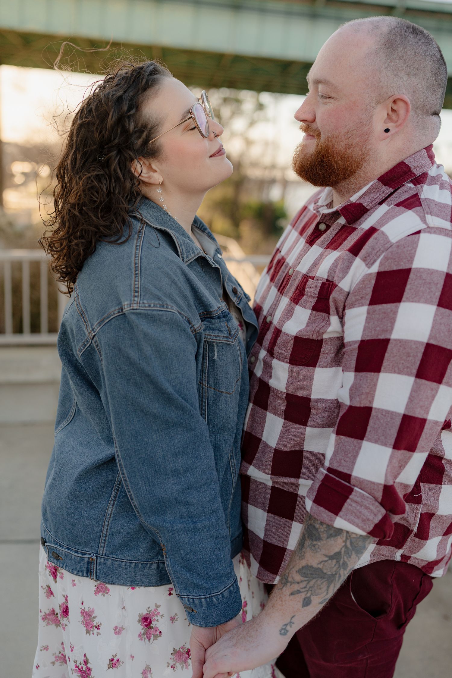 A couple shares an intimate moment outdoors, with one wearing a denim jacket and the other in a red plaid shirt.