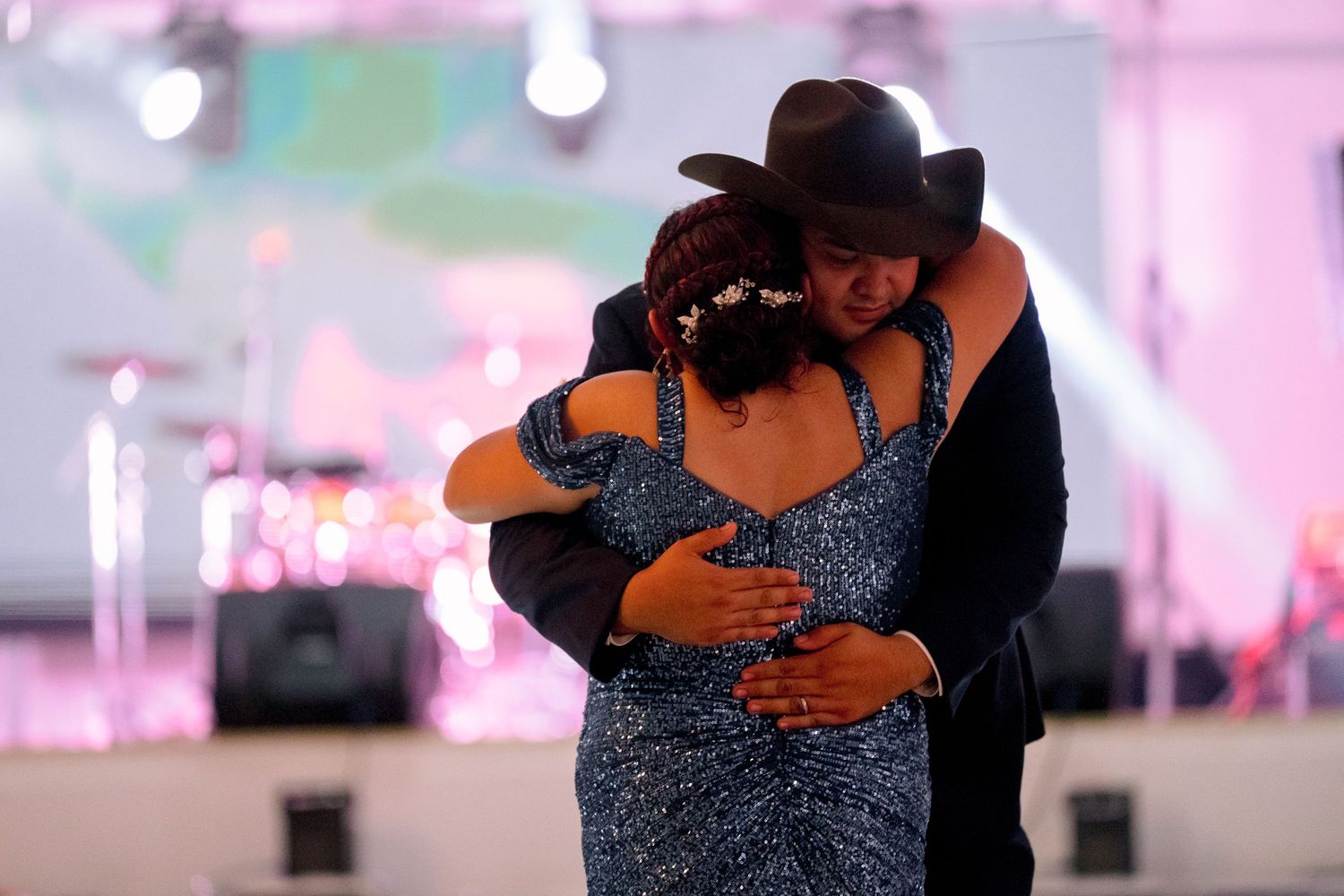 A couple in formal attire dance together in a dimly lit room with pink lighting and romantic ambiance.