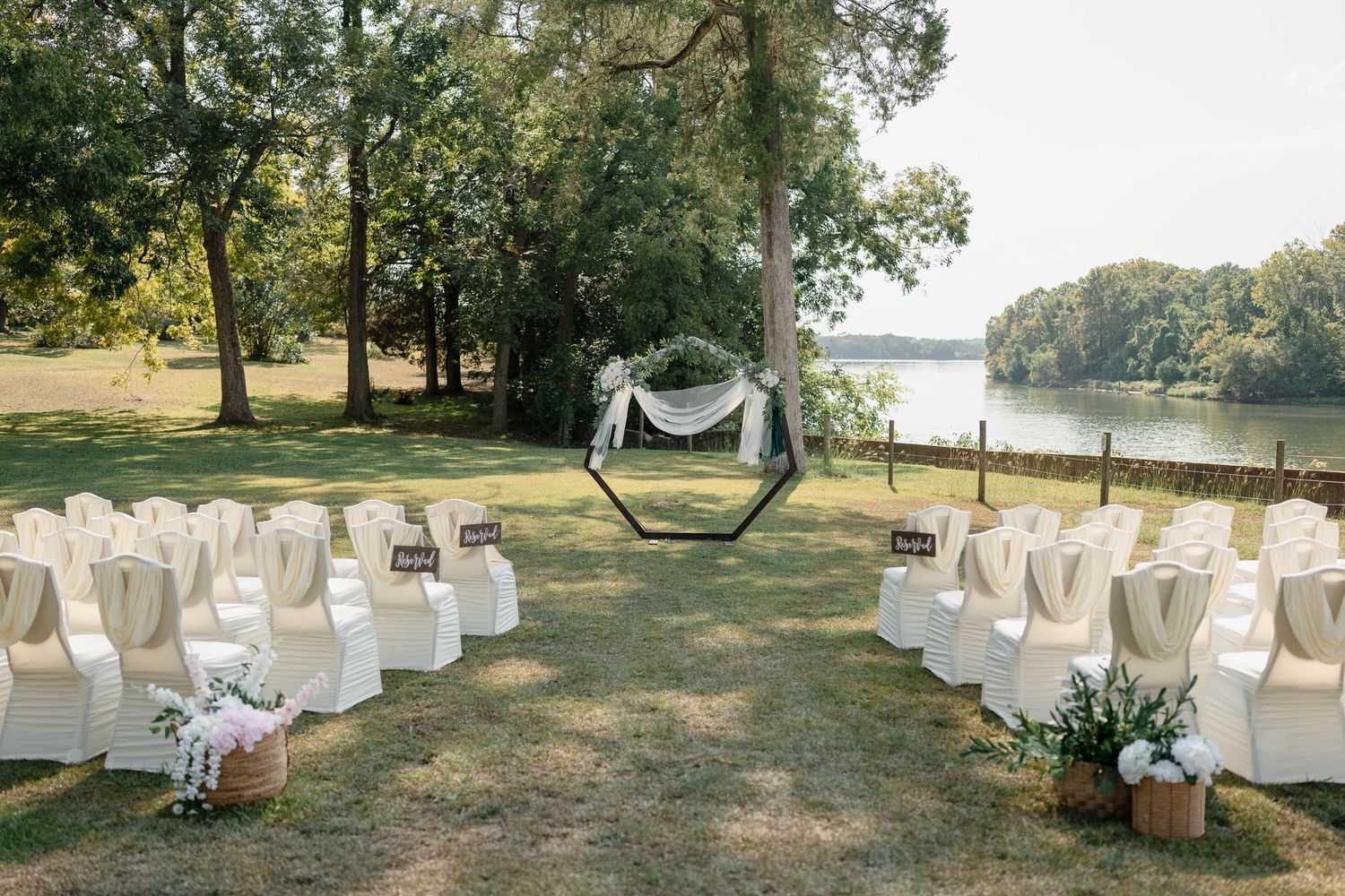 White chairs arranged for an outdoor wedding ceremony near a waterfront with trees in the background.