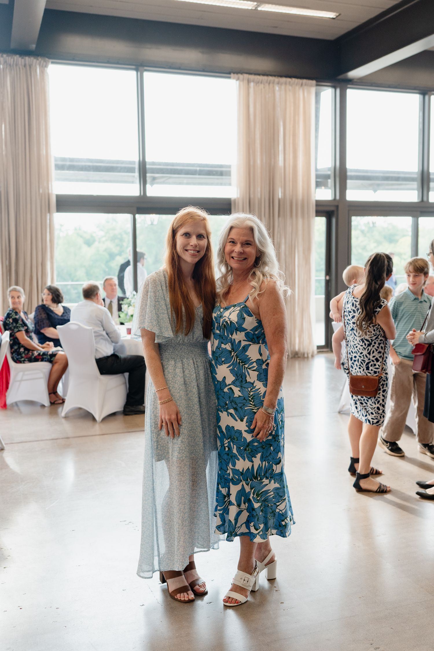 Guests mingle and socialize in a bright modern event space with large windows and white decor.