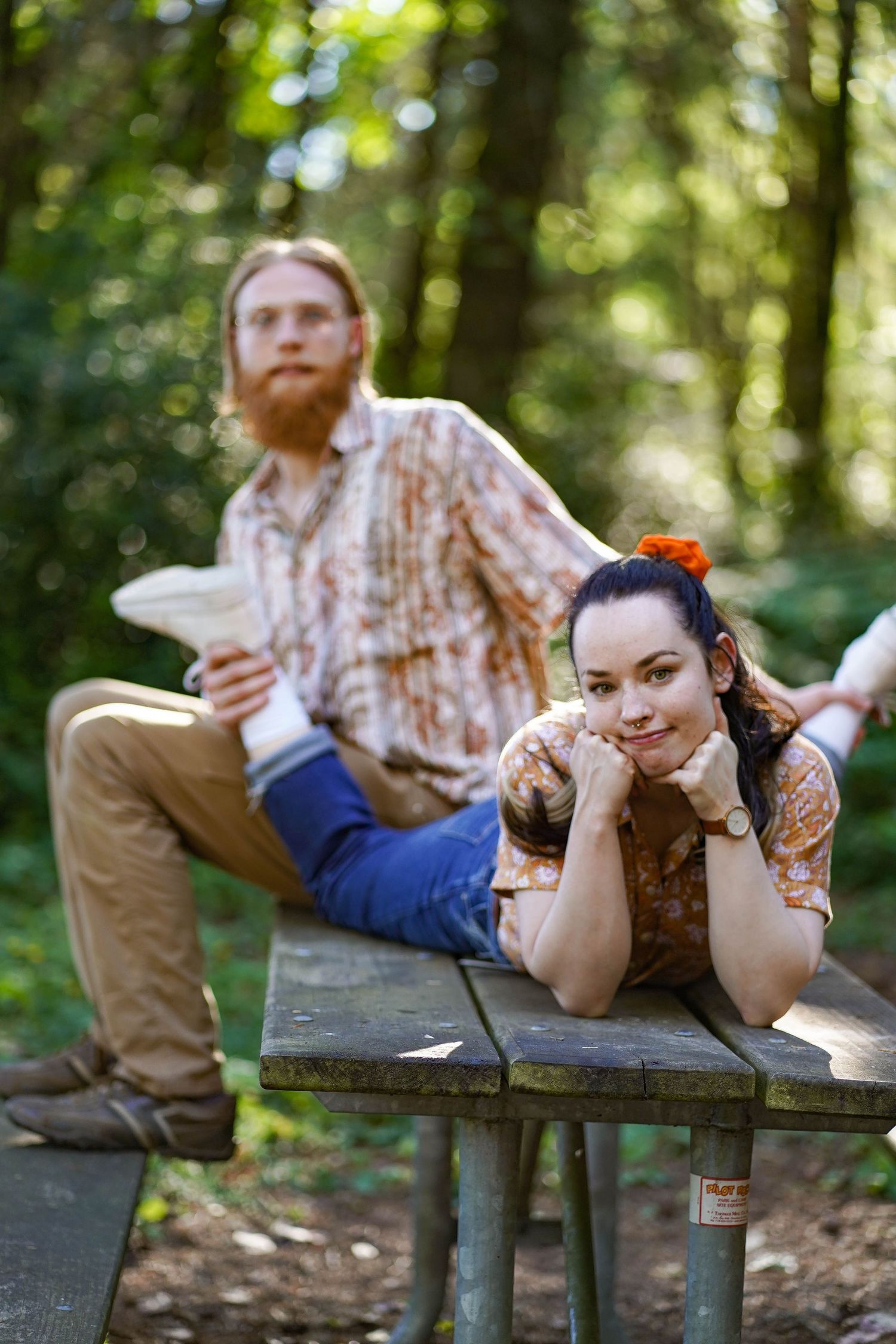 A relaxed outdoor portrait on a picnic bench in dappled forest light.