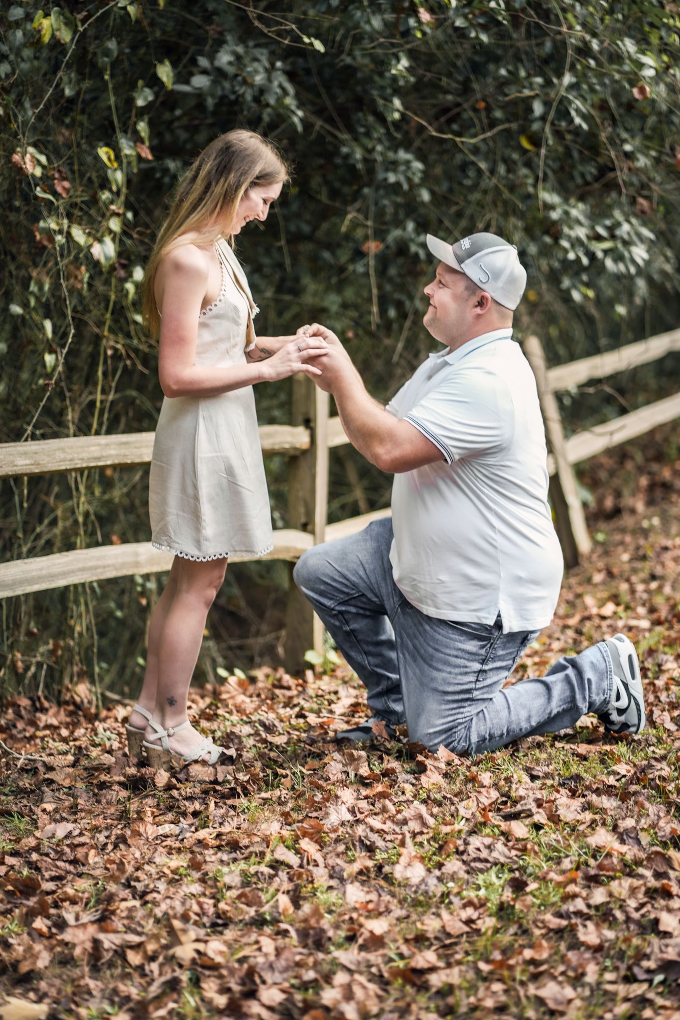 A couple interacts playfully near a wooden fence during their outdoor photo session.