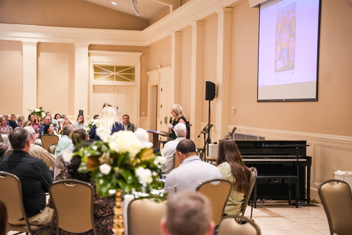 An elegant banquet hall setup with tables, flowers and a presentation screen.