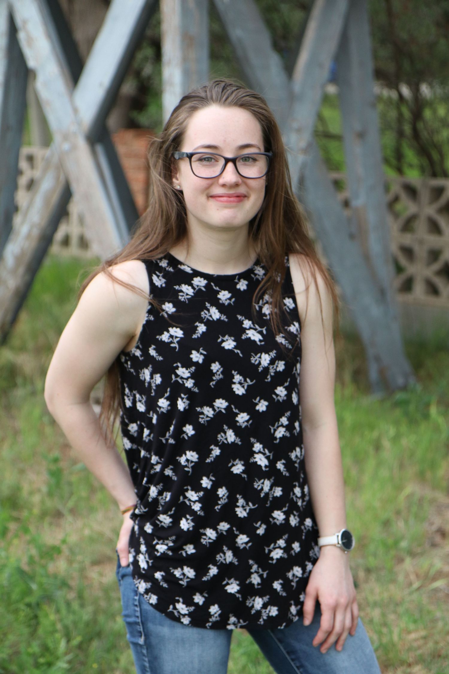 Portrait near wooden bridge structure wearing floral sleeveless top and jeans.