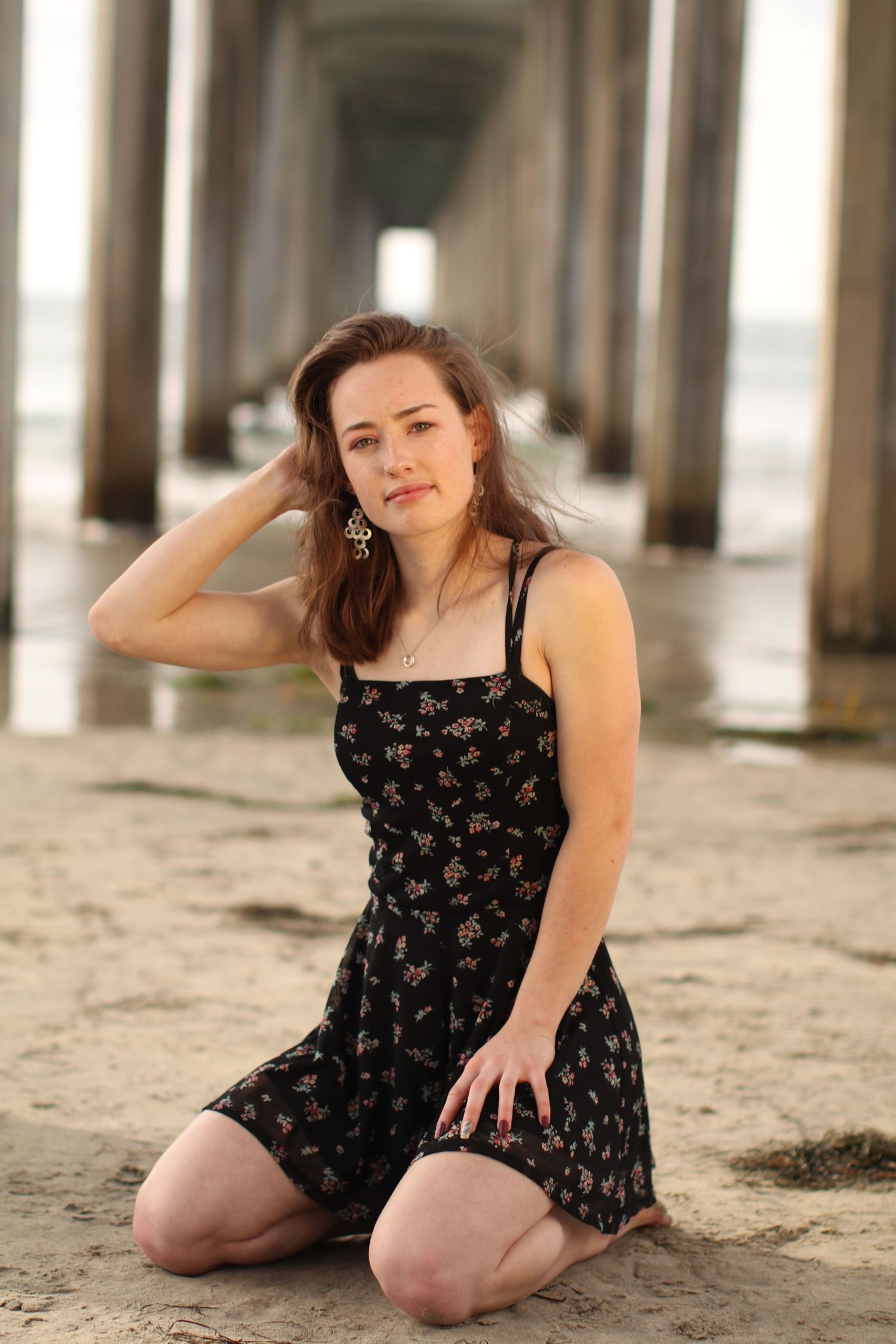 Artistic beach portrait under pier columns in floral summer dress.
