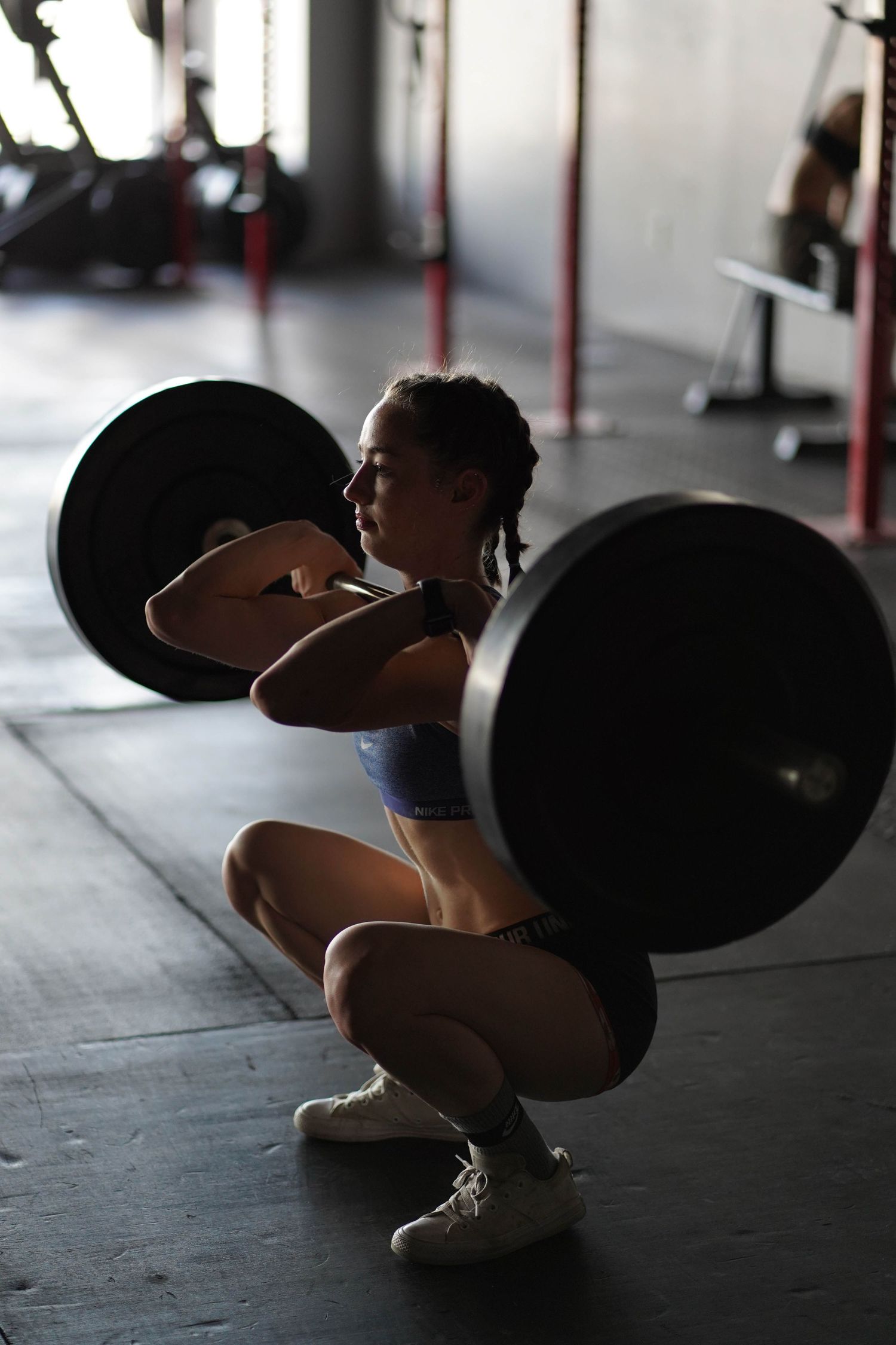 Athlete performing a weighted back squat in a dimly lit gym with exercise equipment.
