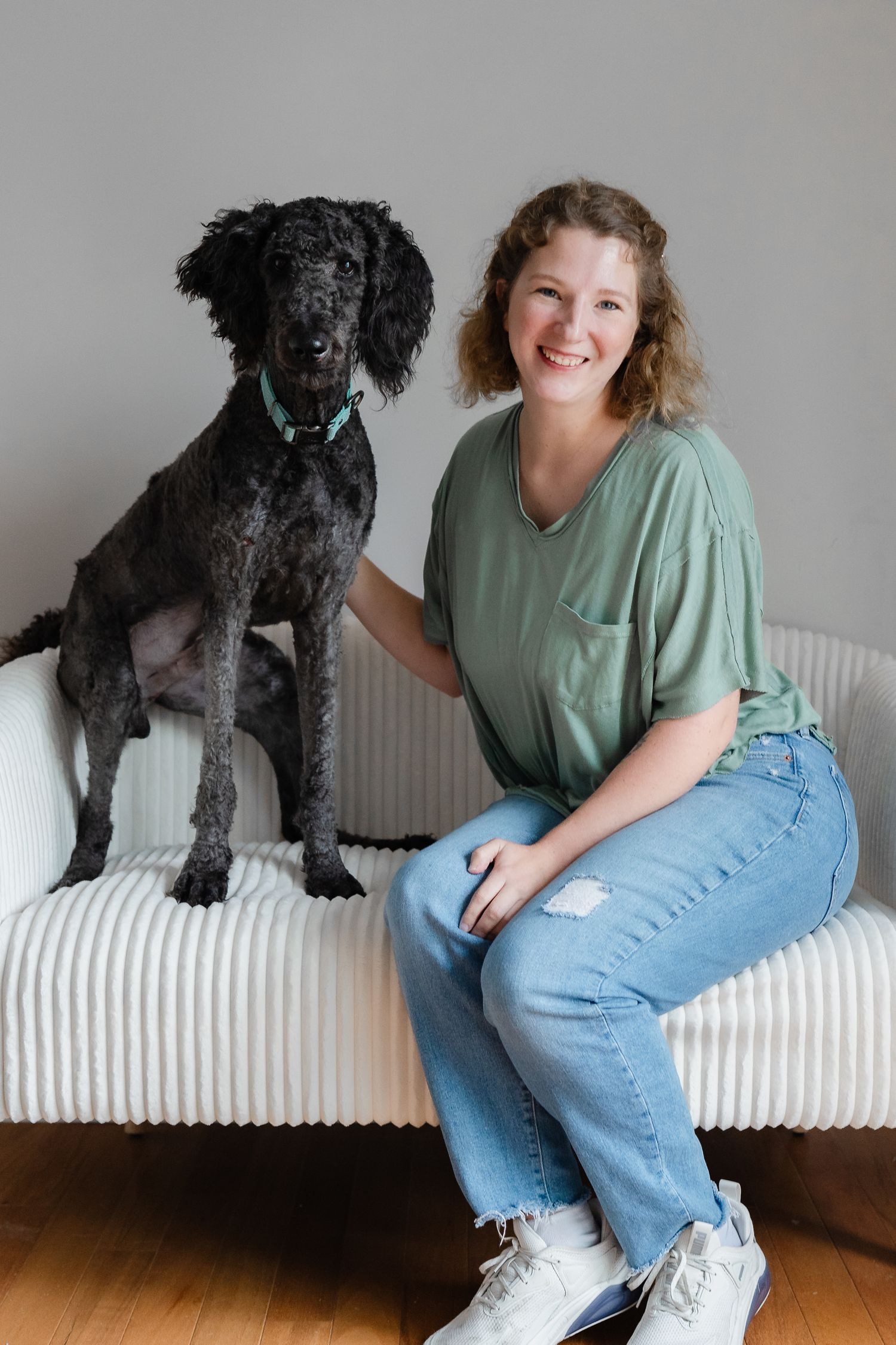 A person in casual wear plays with their black dog on a white couch.