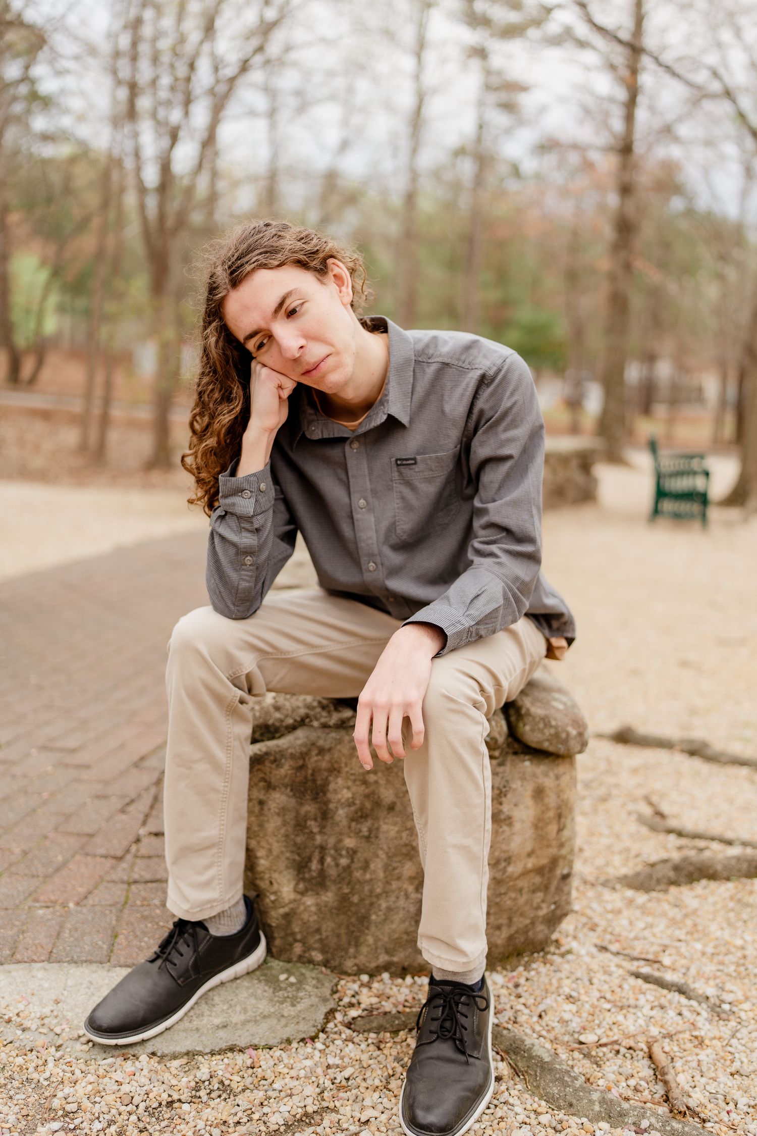 Person lounging on a wooden stump in a forest setting wearing casual attire.