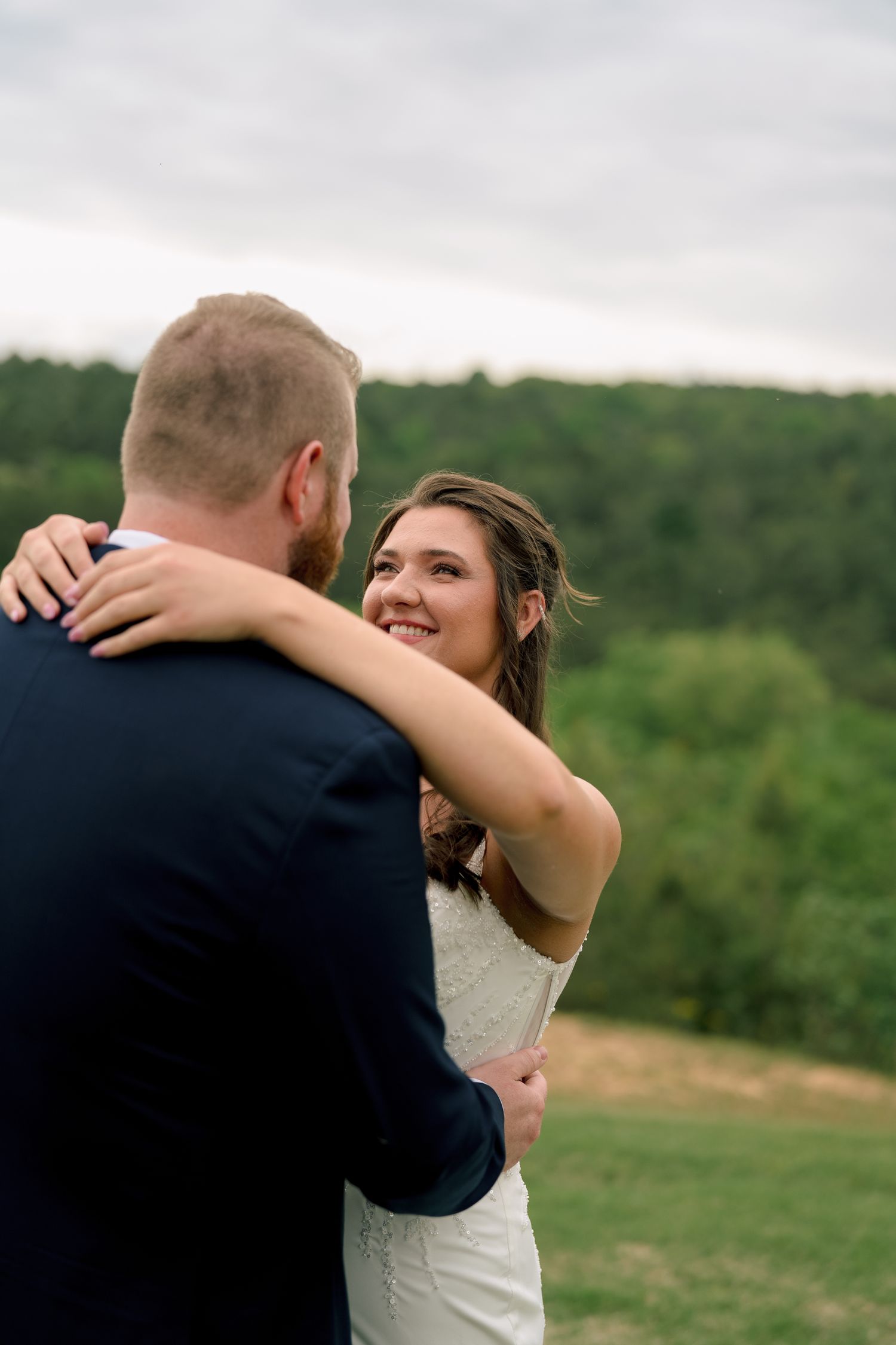 Bride smiling at groom during outdoor wedding portrait with lush green forest backdrop.