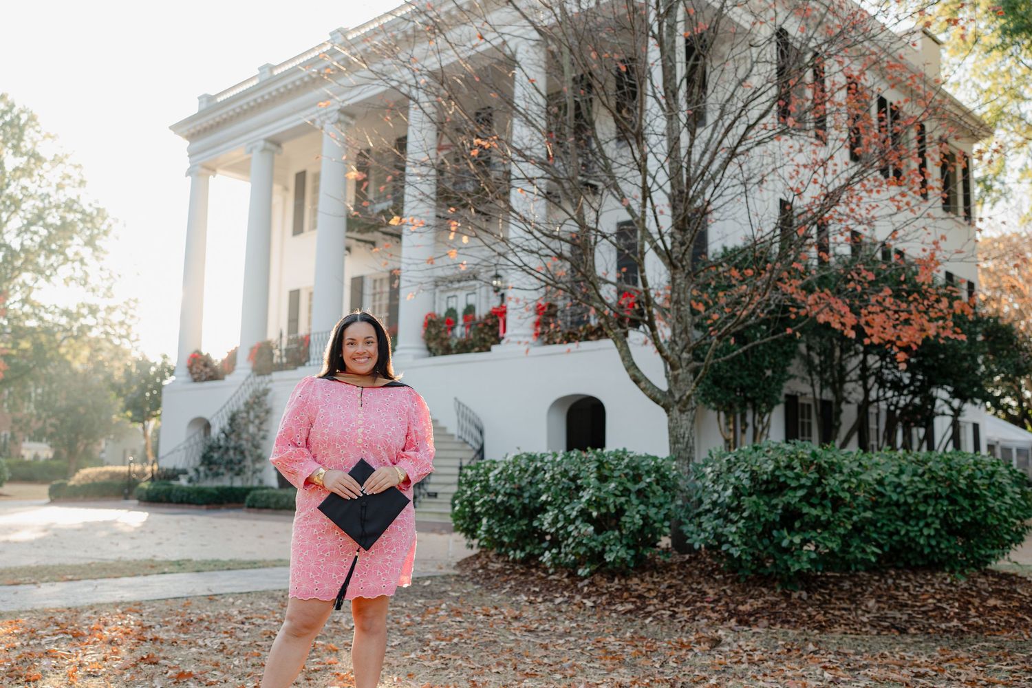 A white colonial mansion with pillars surrounded by autumn foliage serves as a backdrop for outdoor portraits.