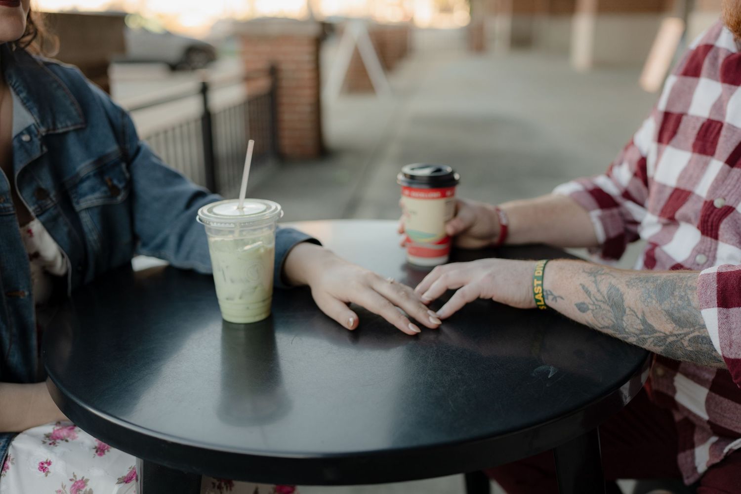 Two people having coffee at a cafe table with disposable cups and a black round table surface.