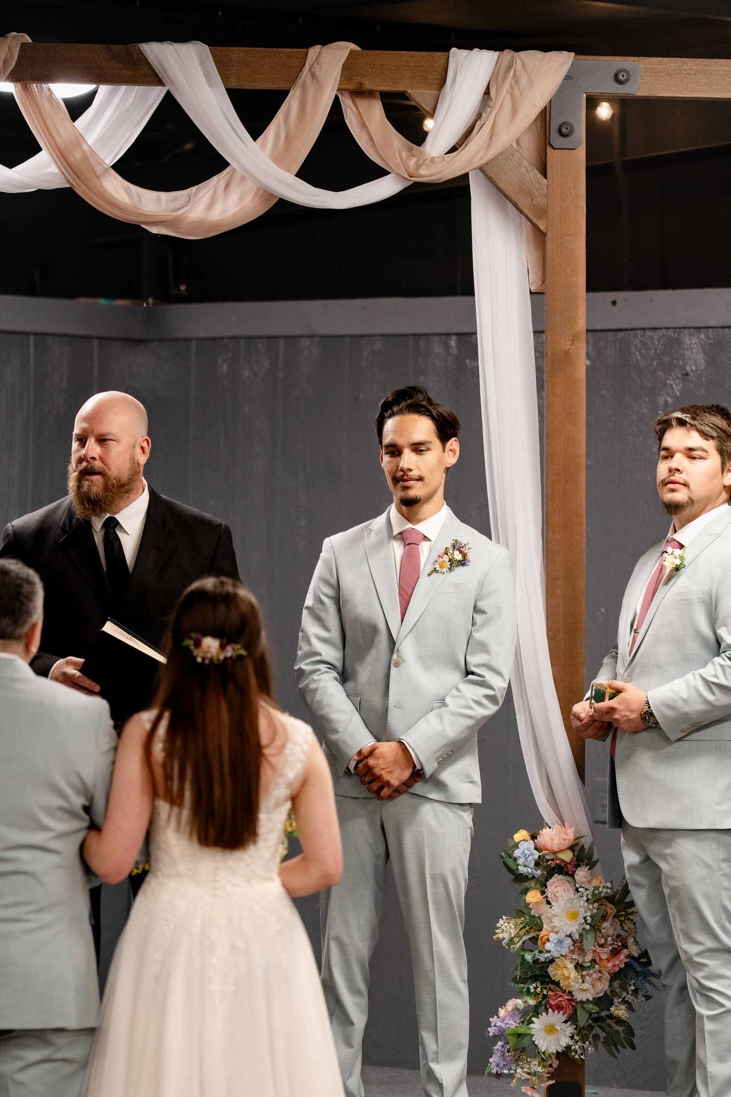 Wedding ceremony in a modern venue with light gray decor and wooden beams overhead.