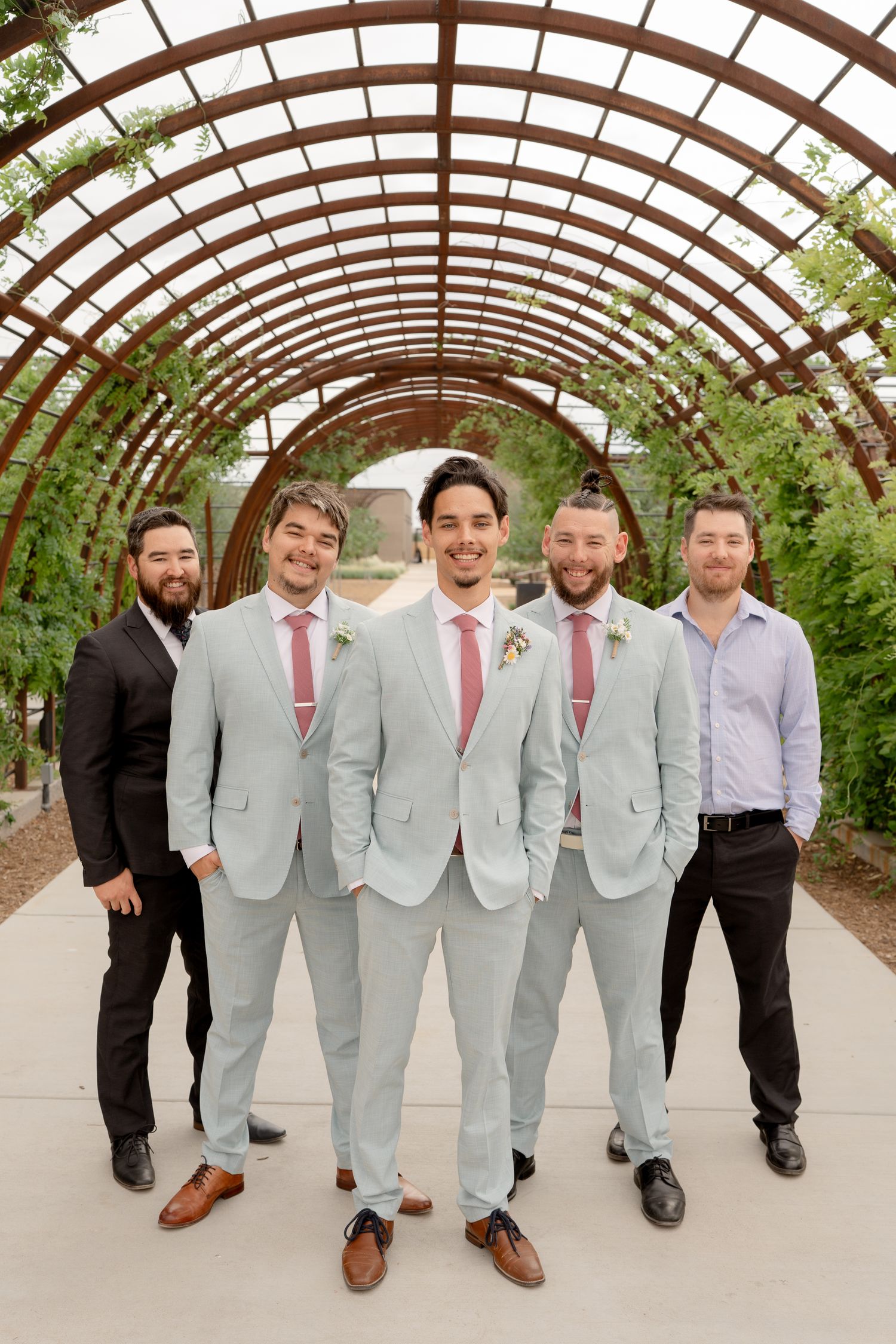 A group in light gray suits and burgundy ties poses together under an arched garden pergola.