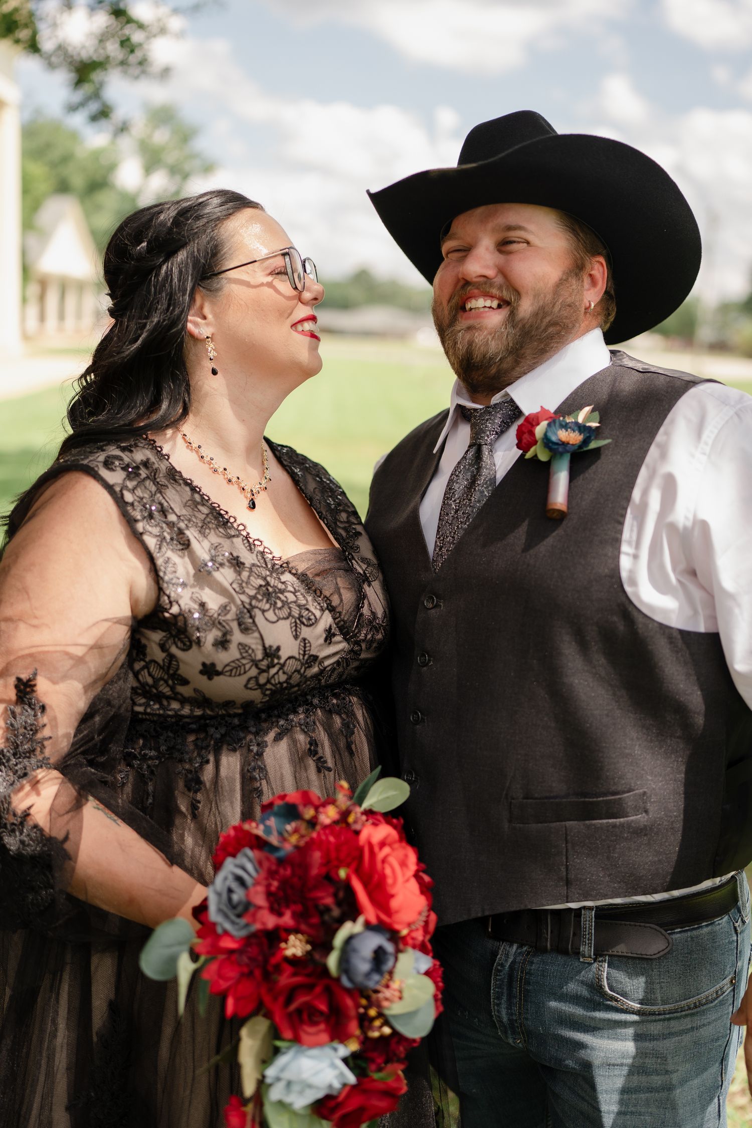 A couple in black western wedding attire shares joyful laughter during their outdoor photo session.