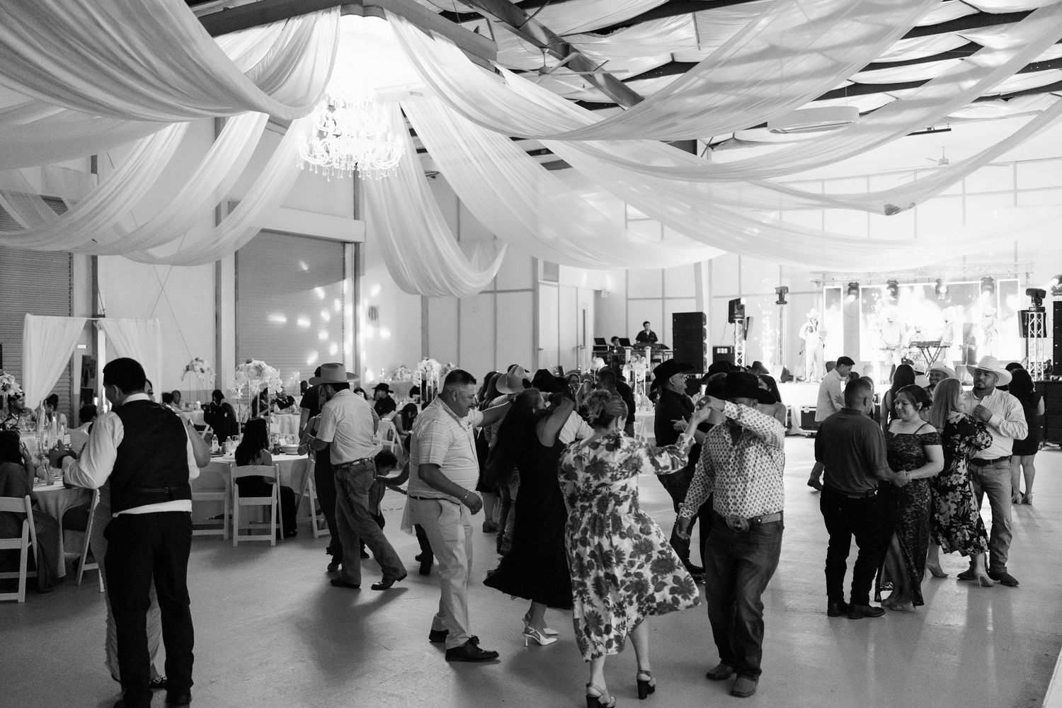 Elegant white draped ceiling and decor in a spacious wedding reception venue with guests.