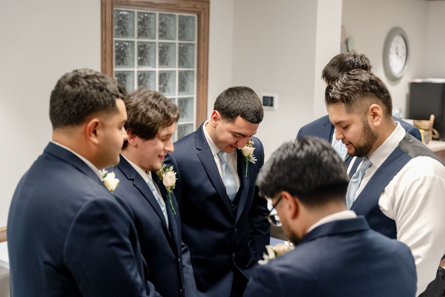 Groomsmen in navy suits gather around a table while getting ready for a wedding ceremony.