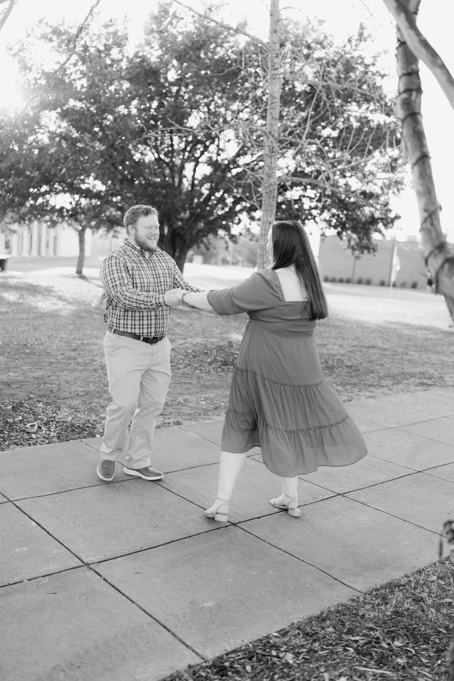Black and white photo of couple dancing playfully on a sidewalk during outdoor engagement photos.