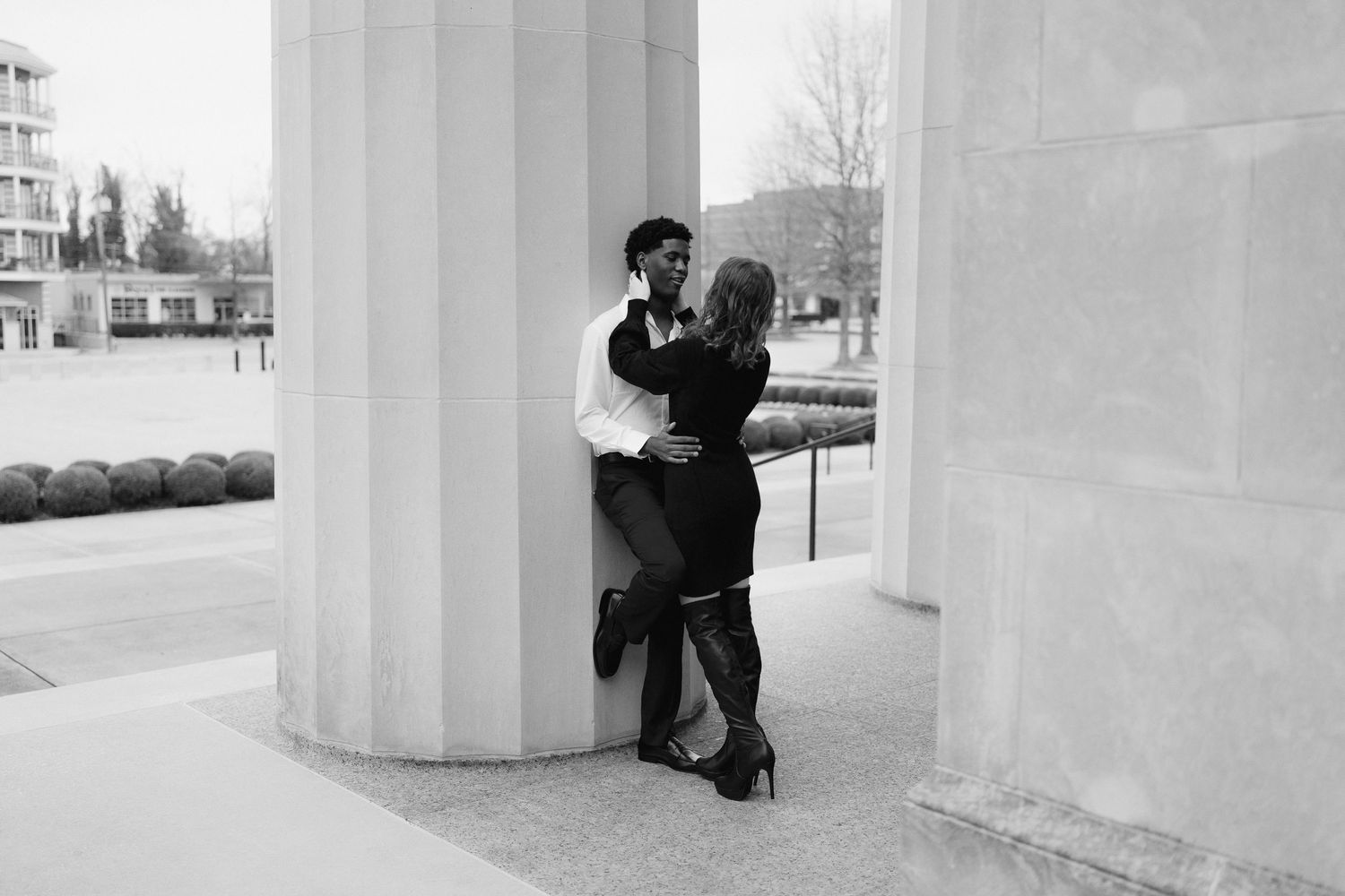 Black and white photo of a couple sharing an intimate moment leaning against large white columns.