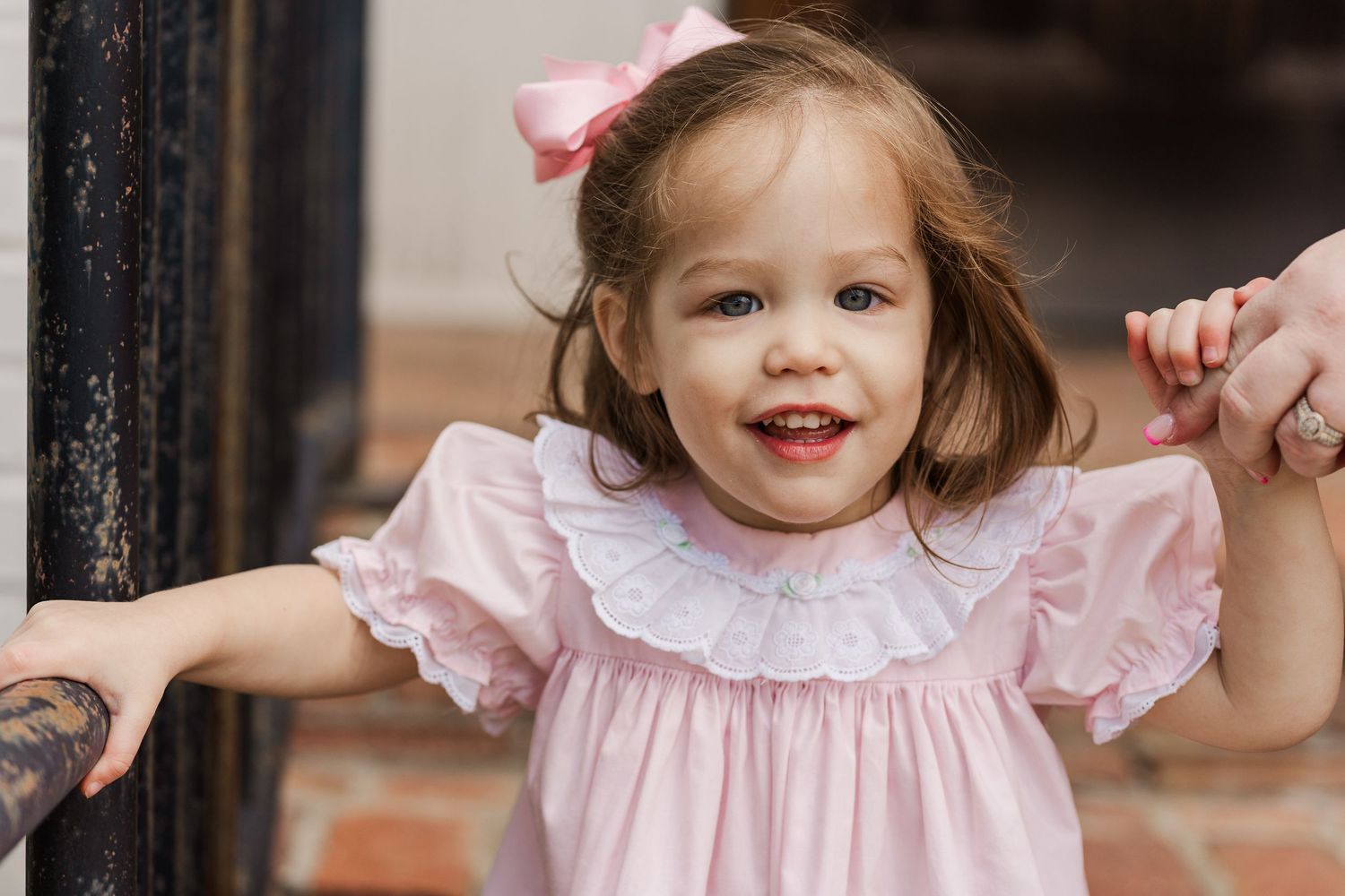 Close-up of child in pink dress smiling while holding railing on brick steps.