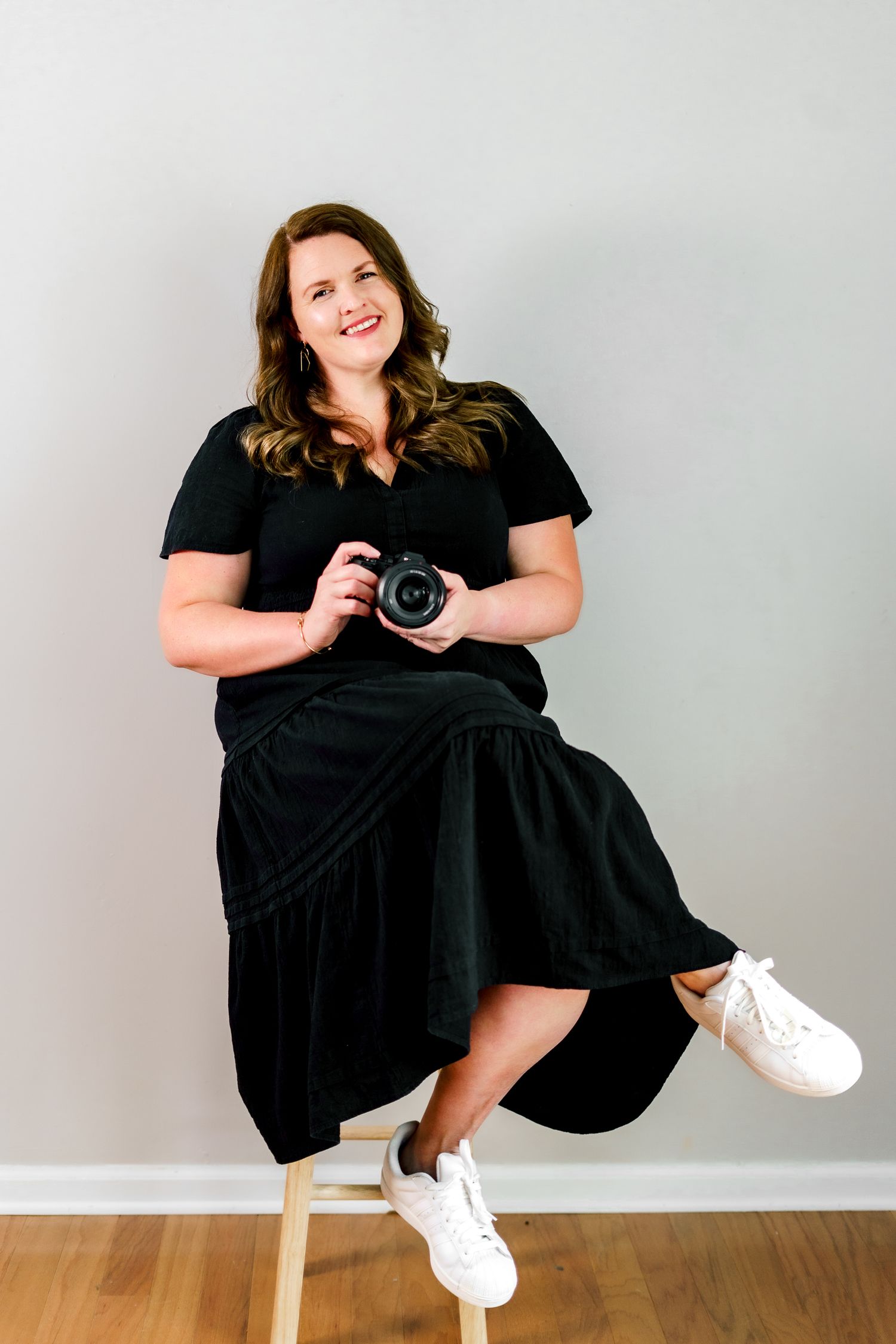 A photographer demonstrates various sitting poses while holding a camera on a white bench.