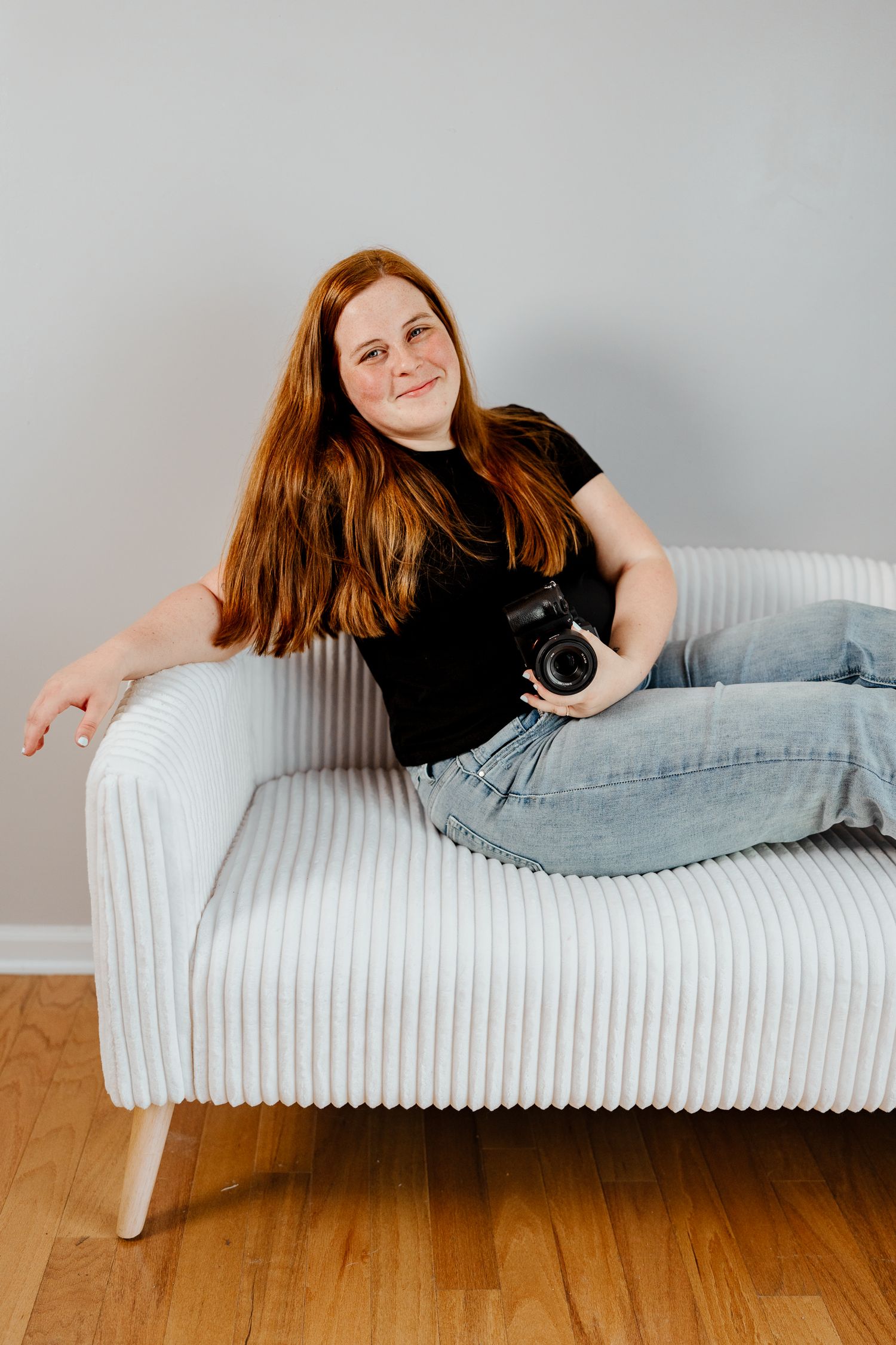Model in black shirt reclining on white contemporary couch during photo session.