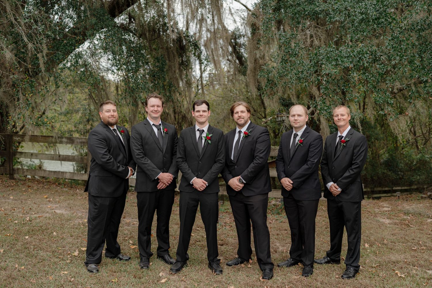 Wedding party in formal attire poses together under weeping willow trees.