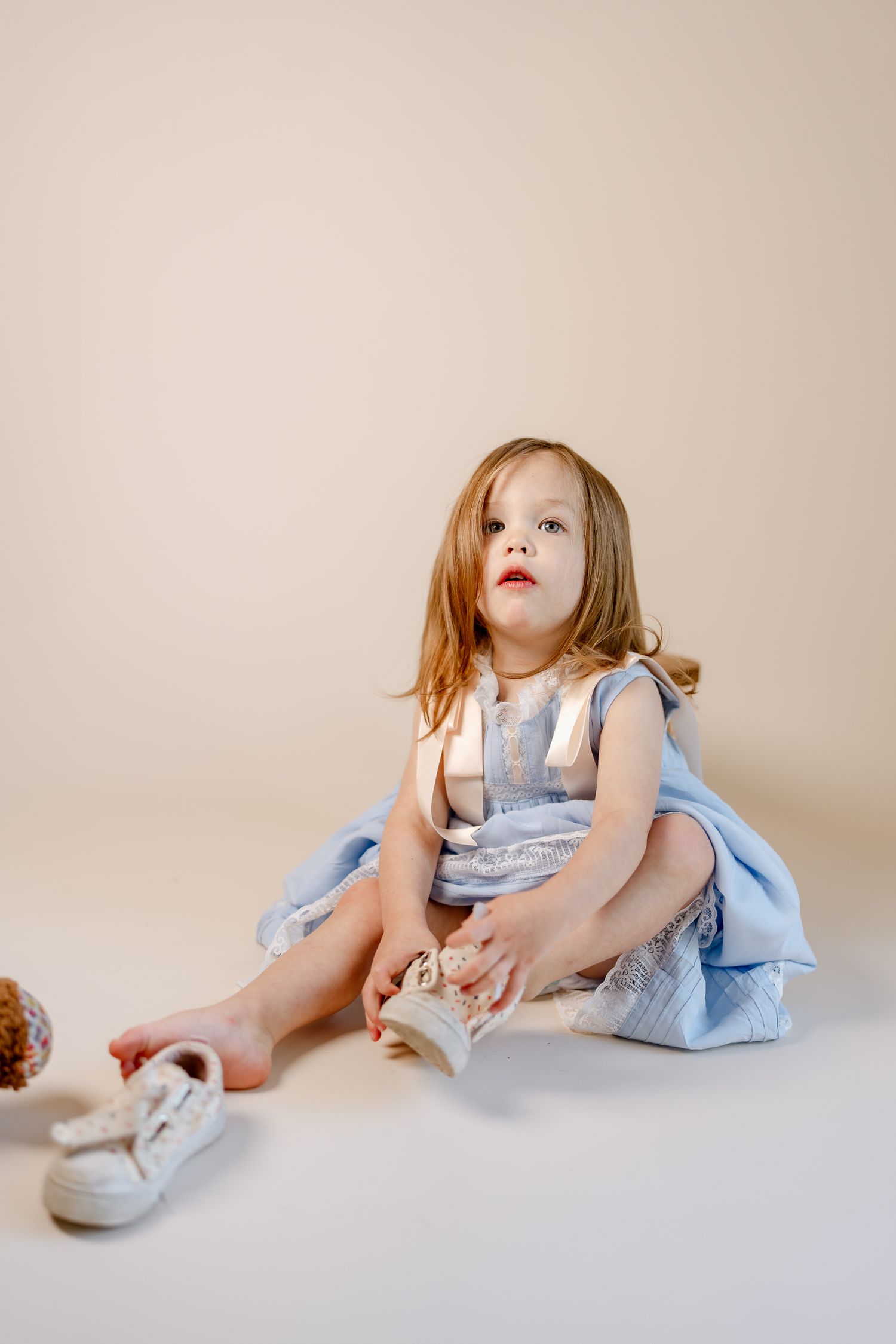 A light blue dress is styled with white shoes in a minimalist studio setting.