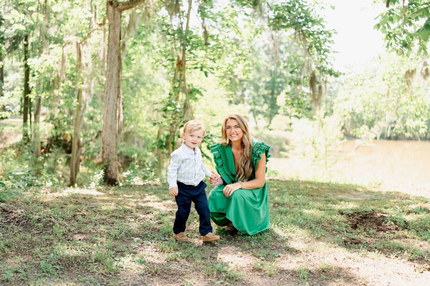 Playful family photoshoot in a wooded area with dappled sunlight filtering through trees.