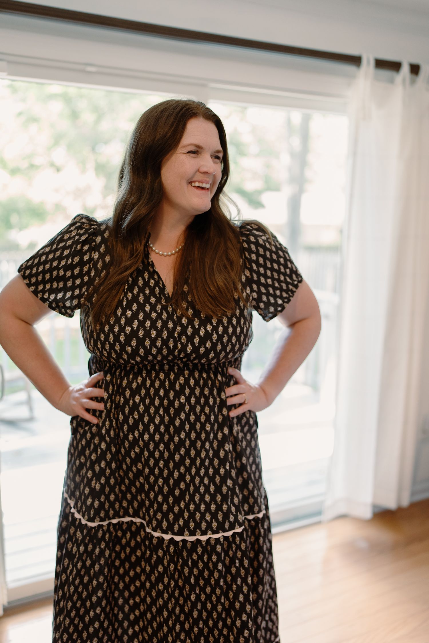 A plus size model wearing a black and white patterned midi dress poses playfully in a bright indoor setting.