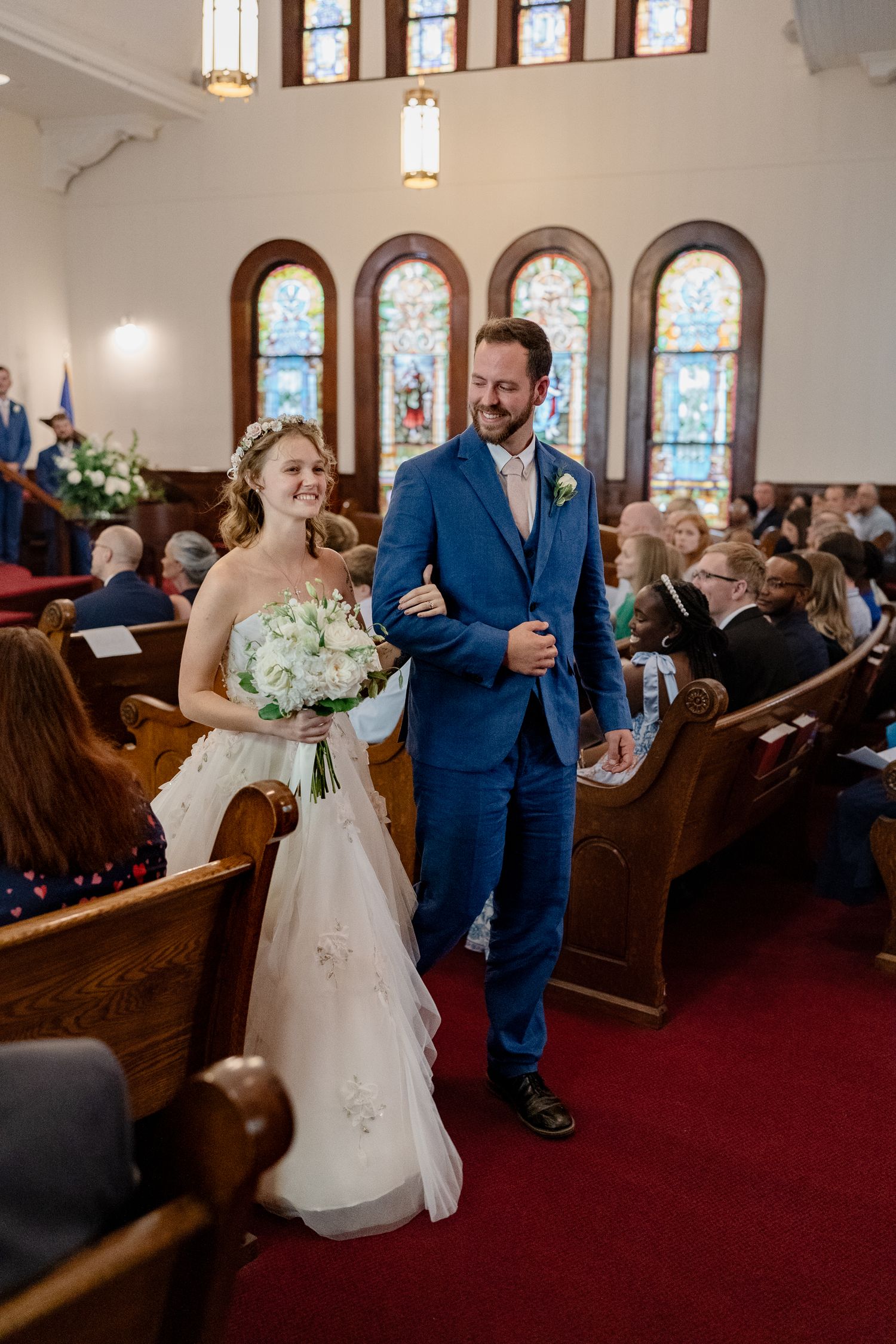 Wedding ceremony in progress inside a church sanctuary with red carpeting and wooden pews.