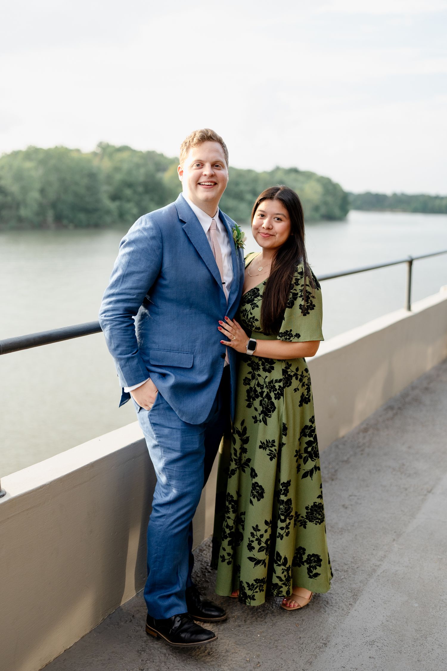 A couple poses together on an outdoor terrace overlooking a scenic waterfront view.