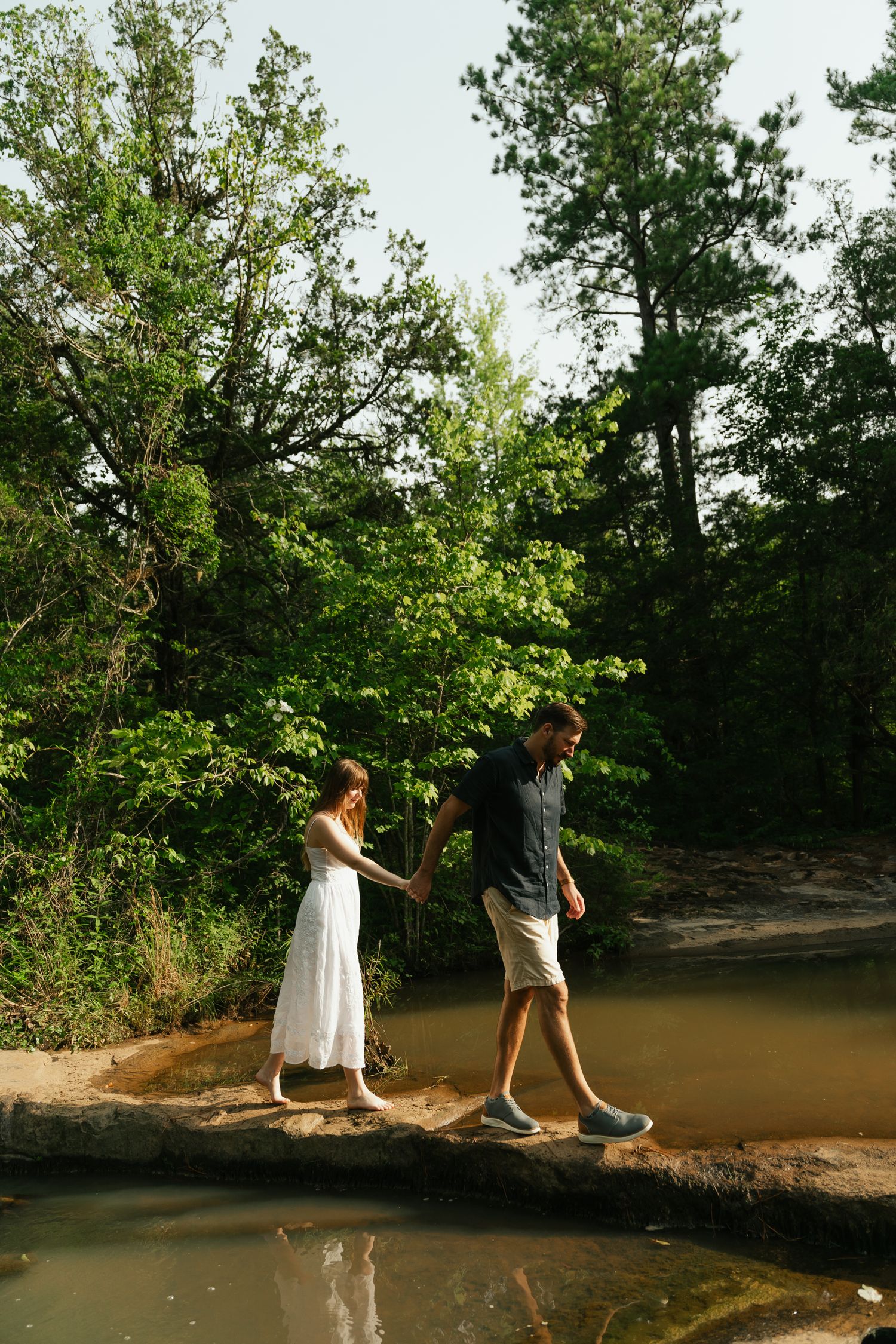 couple walking across a rock with water below them, theyre holding hands