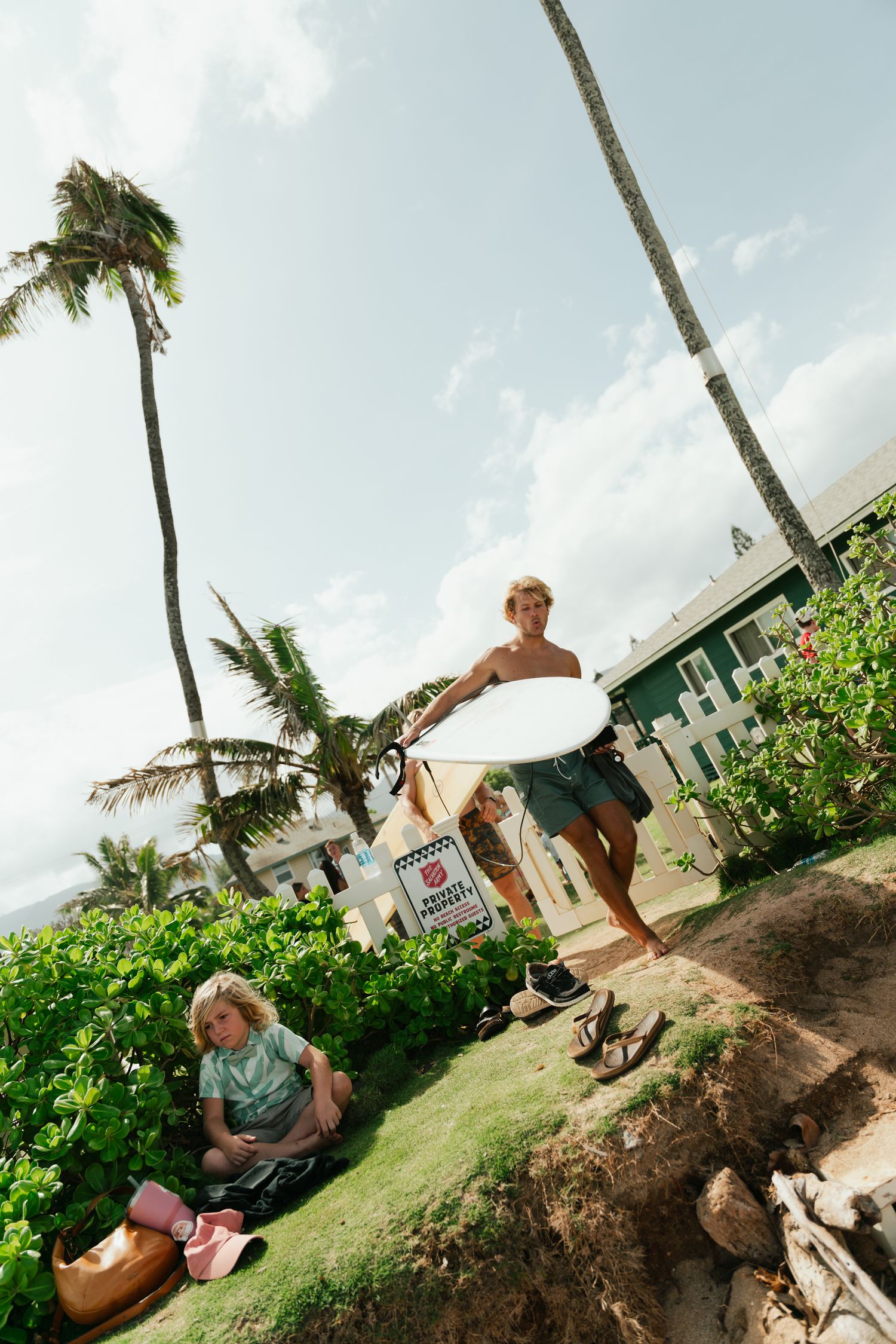 surfers walking to surf, kid sitting in a bush