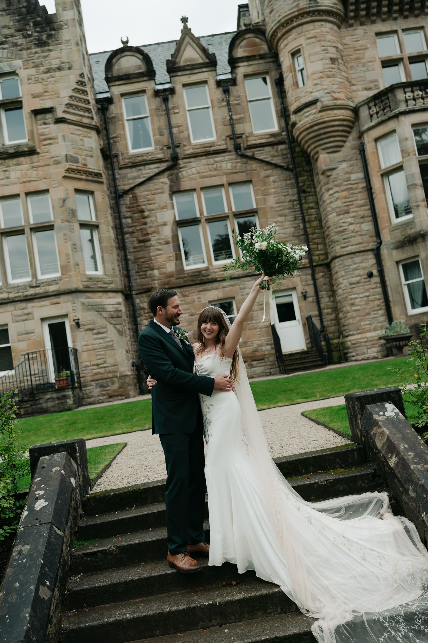 bride and groom standing on steps in front of a castle