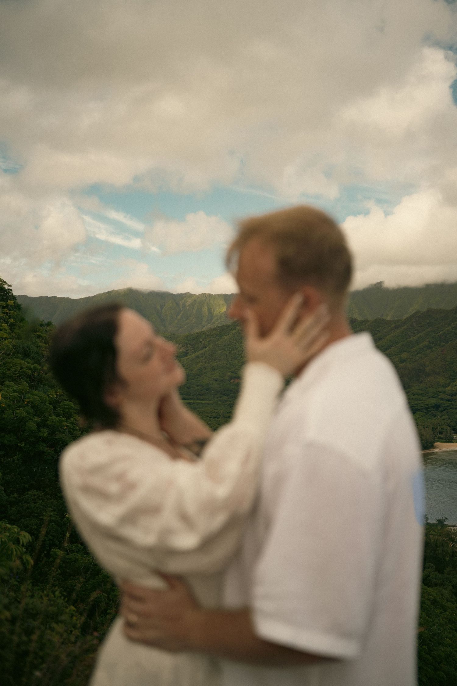 bride and groom out of focus holding each others cheeks, with mountains in focus