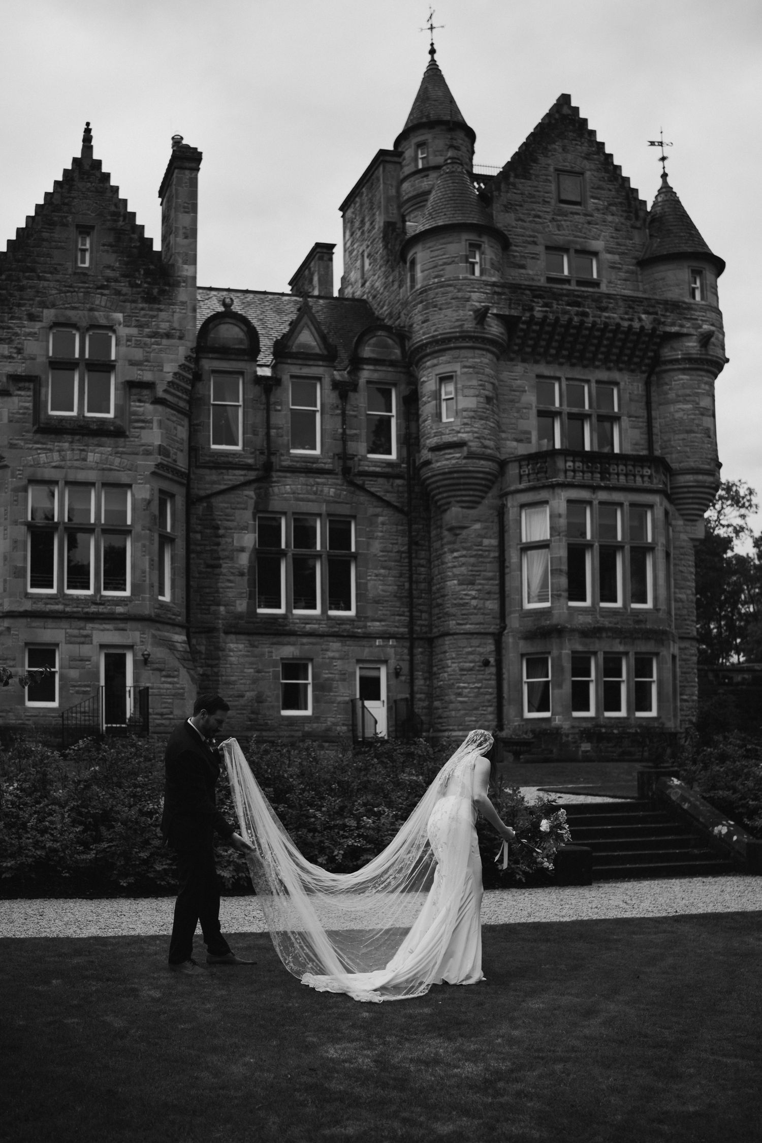bride standing on grass while husband fixes dress
