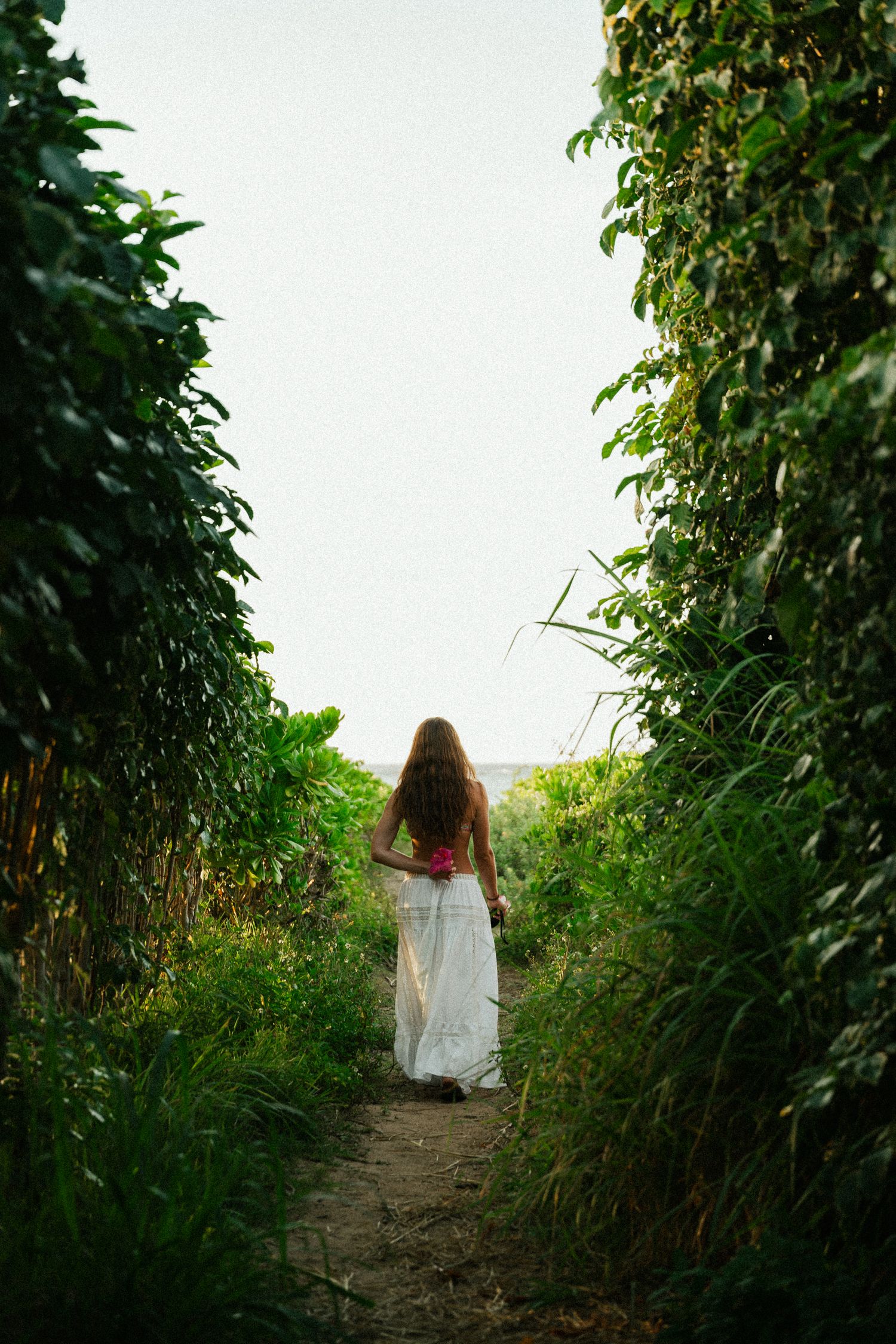 girl walking towards beach with a flower behind her back