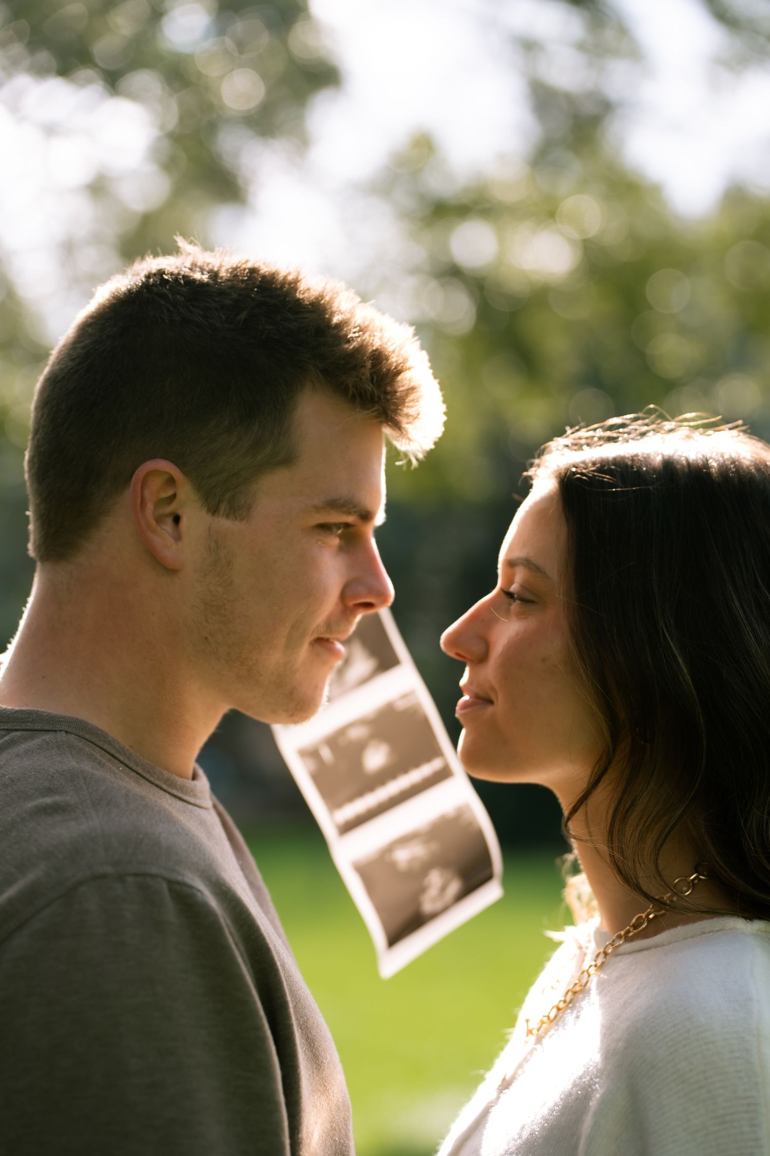 couple staring into each others eyes with pregnancy announcement in the back