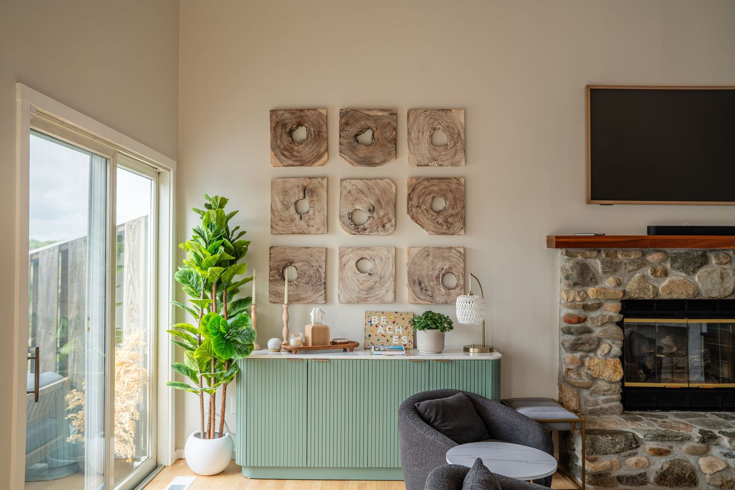 Modern coastal living room features stone accent wall, mint green cabinet, and large windows overlooking the ocean.