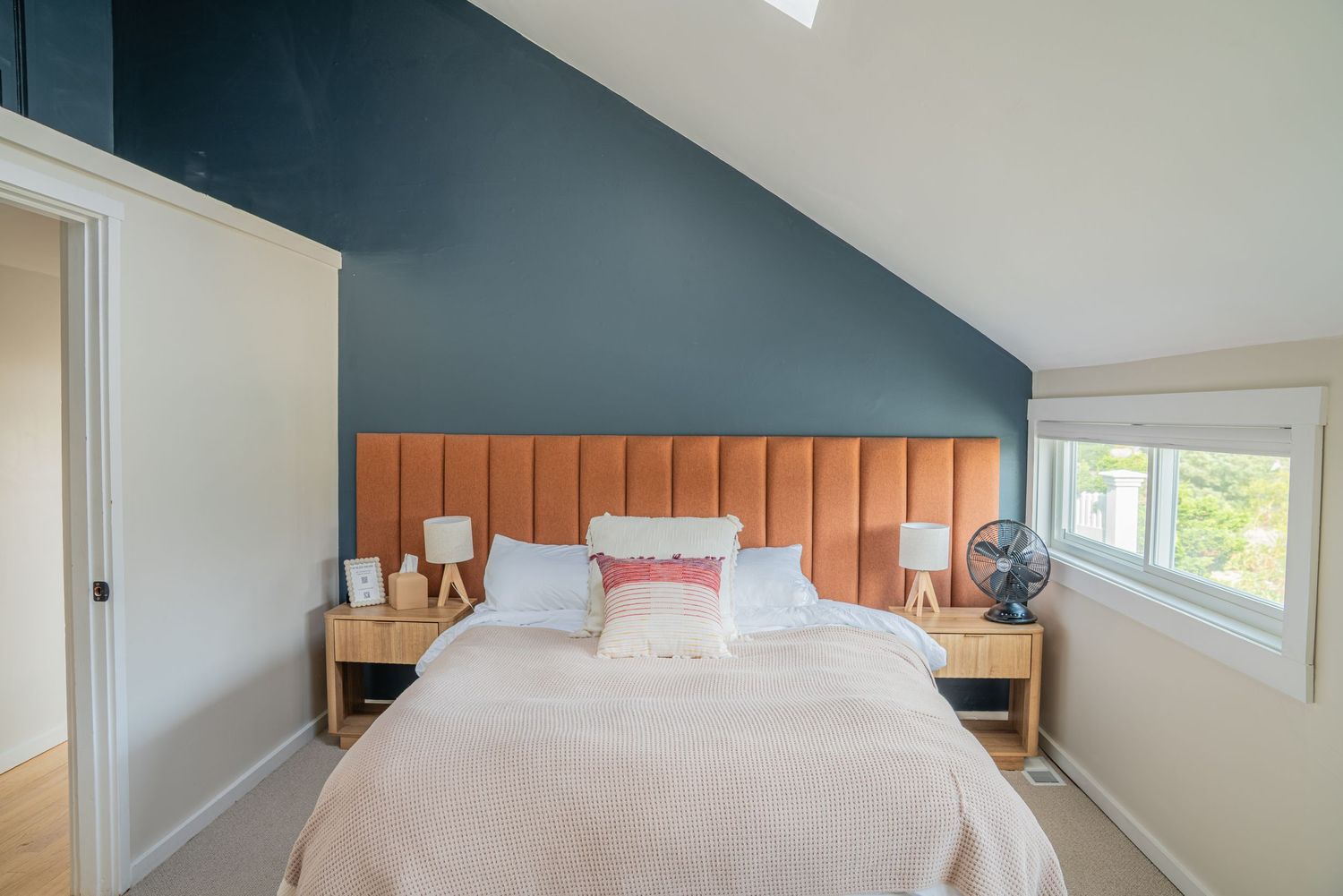 Modern bedroom with vaulted ceiling features teal accent wall and orange upholstered headboard with white bedding.