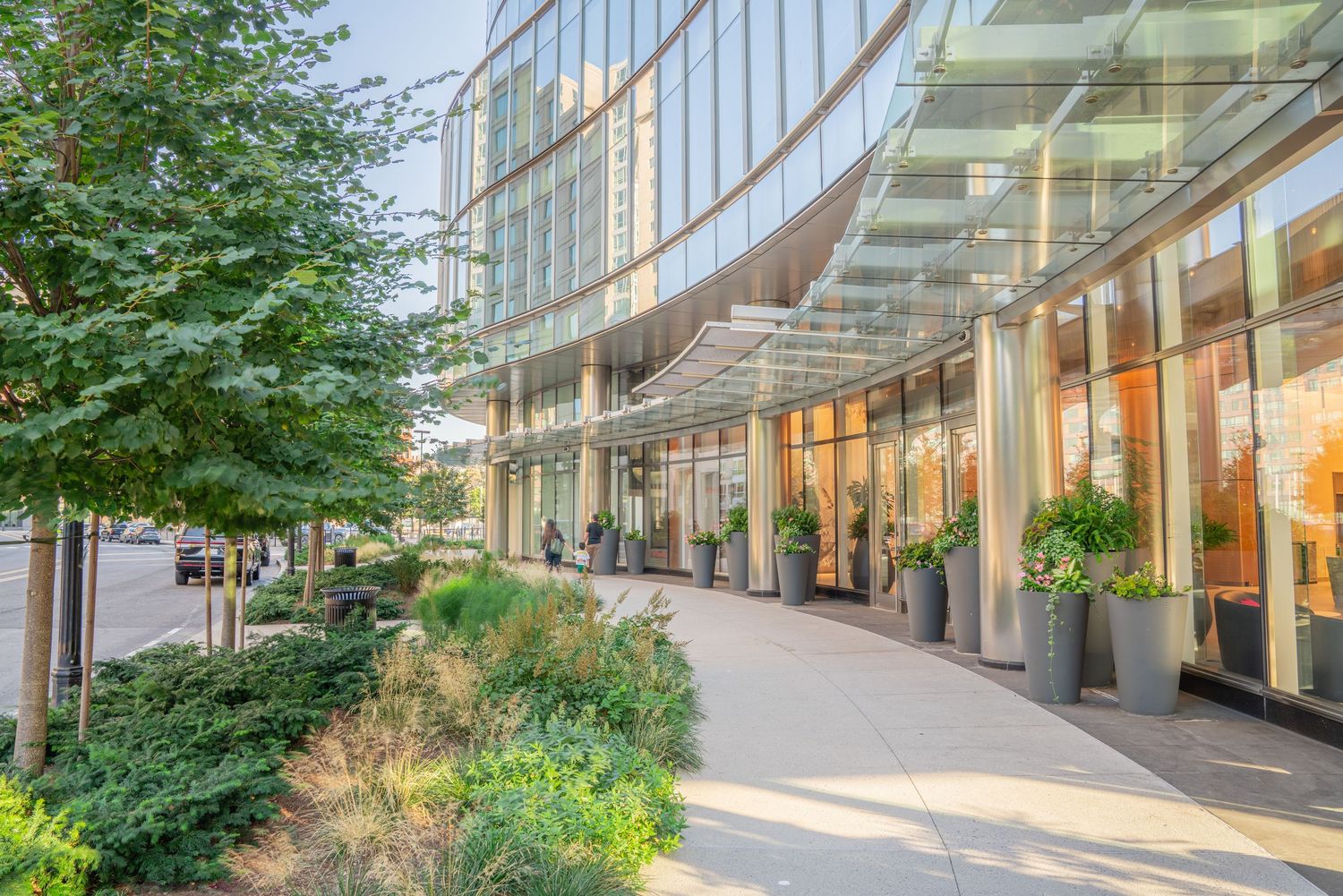 Curved glass facade of modern building with pedestrian walkway and green landscaping.
