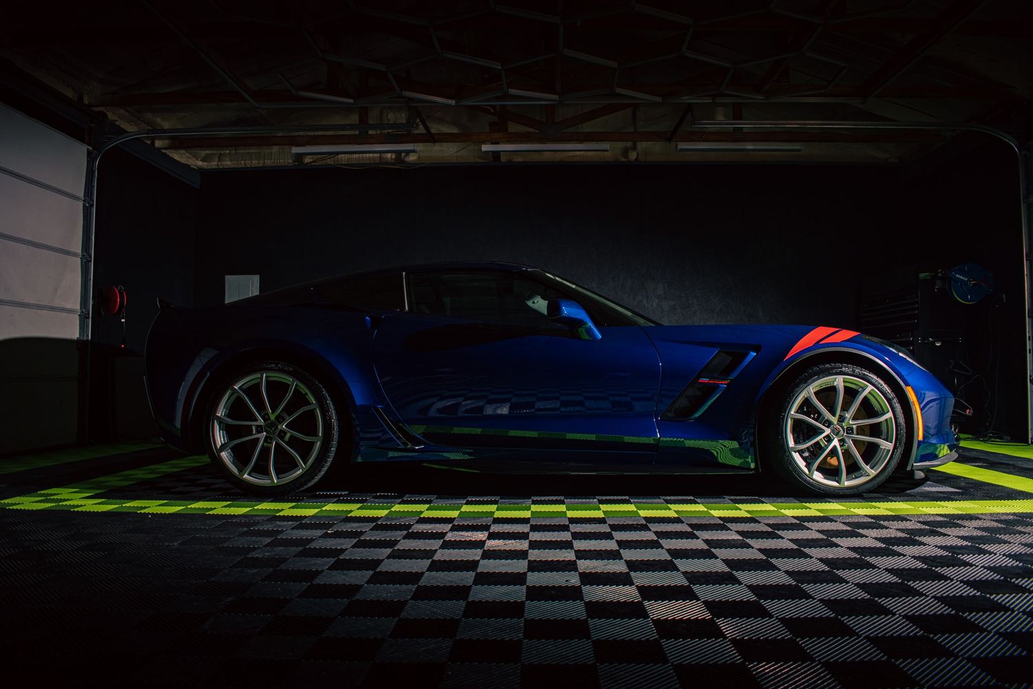 Moody automotive photography of a blue Chevrolet Corvette, captured in dramatic garage lighting with sleek lines and bold performance style.